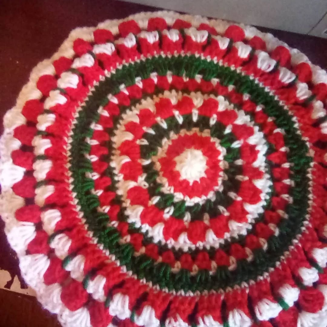 The Crochet Christmas Mandala Place Mat is a festive addition to your holiday decor, featuring a multicolor design perfect for the Christmas season. Made from a combination of cotton and acrylic, this round placemat is adorned with a crocheted pattern, adding a touch of handmade charm to your table setting. With the red heart brand behind it, you can trust in the quality and craftsmanship of this unique and eye-catching piece. Ideal for adding a sprinkle of Christmas cheer to your dining experience, this place mat is sure to be a favorite in your kitchen or dining room.