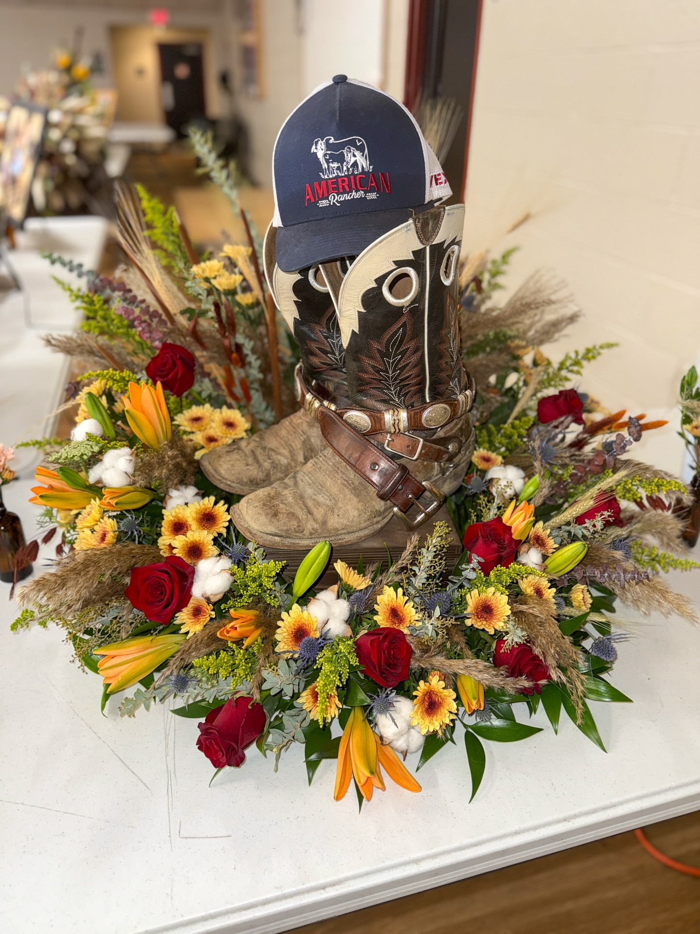 It is always an honor for our team to celebrate someone special we know. Weddings, Funeral, Birthdays, Baby showers, and more! This special occasion hit a little harder than usual. Our dear friend Charlie, has gone home where he is pain free, reunited with so many, buying horses, working cattle, getting work done in the skid loader and mostly importantly cracking some impressive jokes.
Our team held tremendous pride when making these beautiful arrangements. There is nothing more meaningful than incorporating your loved one’s personal items into the designs. Charlie’s lasso was designed with the cross piece, his (extremely heavy) boots, belt and favorite hat placed on a small stand with flowers around, his urn with a rustic floral tribute and the most show stopping piece, a dried arrangement placed on top of his horse saddle.
Charlie, you are missed already but we’re thankful you’re no longer in pain. We’re so proud of you, your accomplishments, and the life you built. We promise to keep things under control down here! Until we meet again. 🕊️🌾