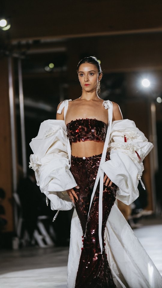 Burgundy sequins. Ivory jacquard. A bow that becomes a statement.
From dressmaking to runway — the Ekin bandeaux and pant set in deep burgundy sequins, paired with the Blaire cape: an oversized bow-shaped silhouette in ivory jacquard, adorned with fabric flowers and crystals found by designer Ou at the Paris Flea Market.
A meeting of chance and intention, where found beauty becomes part of the design story.
This is how a look comes to life.
#OUMAAtelier #EveningwearCouture #RunwayToReality #FashionArtToronto #BehindTheScenes