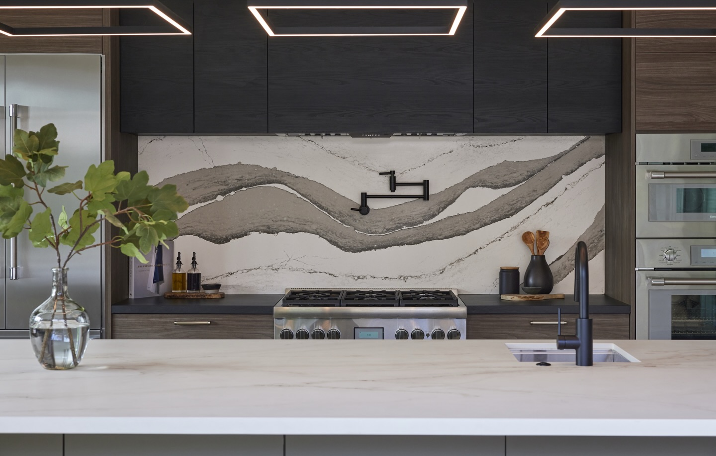 A quiet kind of drama.✨ For our Modern Respite kitchen we let one bold element do the talking — a veined stone slab backsplash that flows like ink across the wall, anchoring the composition while the rest of the palette stays calm and exact. Matte black fixtures, a sculptural pot filler, and deep upper cabinets bring modern edge; warm wood lowers and a serene island countertop keep it grounded and livable.
This is how function meets serenity: generous prep space, thoughtful storage, and moments of material poetry — designed for everyday cooking, efficient entertainment, and slow mornings with a cup of coffee.
Interior Design: @sonomainteriors
Photography: @luiscostadonephoto