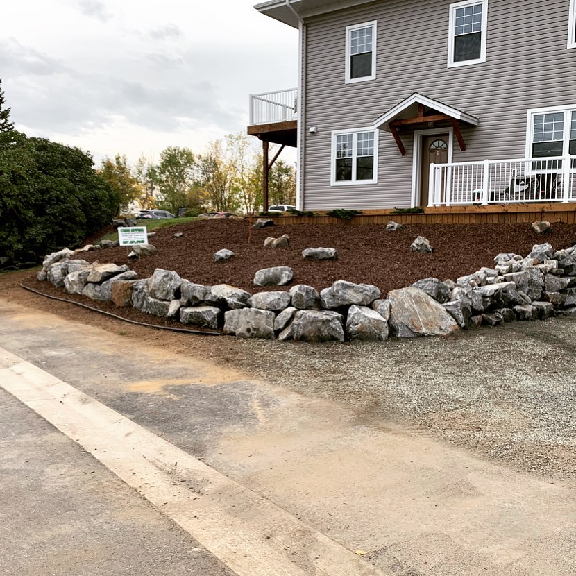 When you mix 20 ton of boulders and 10 yards of mulch together carefully, you can clean up the front of condo building pretty nicely! #maintanancefree#curbappealmatters#rockwalls#curbappeal