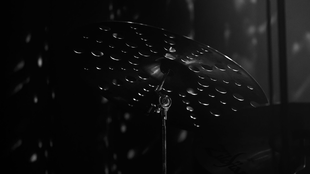 Fotograferen in het donker gaat gewoon niet! Wat ontbreekt er?
Licht! Fotograferen is op zoek gaan naar de grens tussen: spelen met licht en manipuleren van licht. Hoe ver kun je gaan met het veranderen van de omgeving. Het beeld moet er vanuit mijn perspectief nog realistisch uitzien. Ik vind het heerlijk om op zoek te gaan naar dat ene object dat het licht vangt en misschien wel weerkaatst of doorlaat.
De techniek in het kort: de sensor van de camera zet licht om in pixels. Hierbij wordt er informatie doorgegeven en vertaald naar losse parameters, zoals: luminantie, saturatie, helderheid, kleur en nog zovéél meer.
Deze cymbal van Zildjian heeft gaten voor de klank waar drummers fan van zijn, maar het ziet er ook ongelooflijk cool uit! Fantastisch dat er door die gaten, ruimte ontstaat voor de glinstering van het licht. Door de diepte tussen het object en de ruimte eromheen ontstaat er een soort mysterie in een cinematografisch jasje.
Vind jij deze look helemaal geweldig en wil jij ook concertfoto's, of detailfoto's van een product on stage? Ik denk graag met je mee!