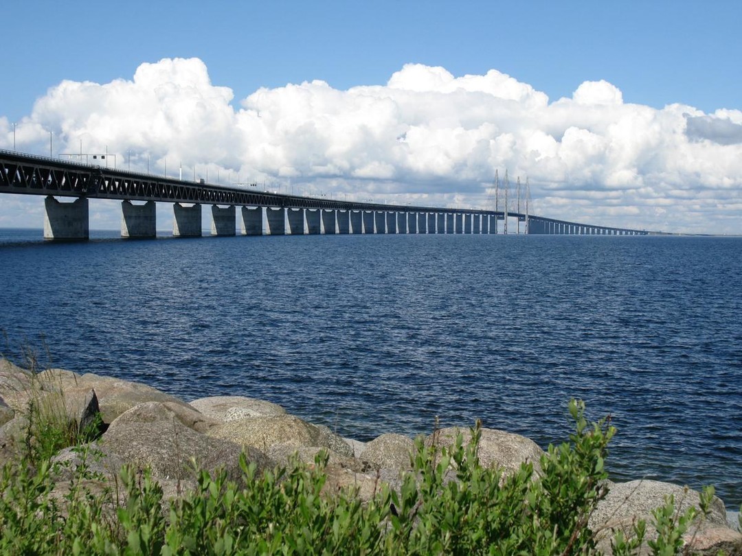 Det är verkligen häftigt att vi på BroLänk tillsammans med Maurer får möjligheten att vara del av underhållet på Öresundsbron, en så pass ikonisk och tekniskt avancerad konstruktion.
Bron har ju en central roll både symboliskt och praktiskt som förbindelse mellan Sverige och resten av Europa.
Här är några faktorer som kan vara intressanta att ta i beaktande under vårt arbete med övergångskonstrutioner.
Övergångskonstrutioner är kritiska eftersom de hanterar rörelser som orsakas av temperaturväxlingar, trafikbelastning, och vind. Med tanke på Öresundsbrons längd och höjd är det viktigt att lösningarna kan absorbera dessa dynamiska krafter utan att påverka brostrukturen negativt.
Faktorer att beakta:
1. Temperaturvariationer: Öresundsbron utsätts för stora temperaturskillnader som kan orsaka termisk expansion och kontraktion. Övergångskonstruktionen måste kunna hantera dessa rörelser utan att orsaka sprickor eller skador.
2. Vindbelastning: Bron, speciellt med sin höjd och öppna läge över havet, utsätts för starka vindar som kan skapa laterala rörelser. Snedkabelkonstruktionen är effektiv, men övergångskonstruktionerna måste också klara av de rörelser som dessa krafter kan orsaka.
3. Materialegenskaper: Eftersom bron är byggd i stål och betong, är det viktigt att materialen i övergångskonstruktionen har kompatibla egenskaper med de befintliga materialen för att undvika korrosion och andra skador över tid.
4. Hållbarhet och livslängd: Ett viktigt mål är att minimera framtida underhåll och förlänga livslängden på bron. Lösningarna som tas fram är långsiktiga och håller hög kvalitet.
5. Säkerhetsaspekter: Trafiksäkerheten är naturligtvis avgörande. Övergångskonstrutionerna måste vara utformade för att minimera riskerna för fordonsolyckor, särskilt med tanke på brobanans längd och höjd.
Konstruktionsdata
Längd: 15,9 km (varav 7,8 km bro och 4,1 km tunnel.
Bredd: 31,5 m
Höjd: 203,5 m
Segelfrihöjd: 57 m
Konstruktionstyp: Snedkabelbro och sänktunnel
Material: Stål & Betong