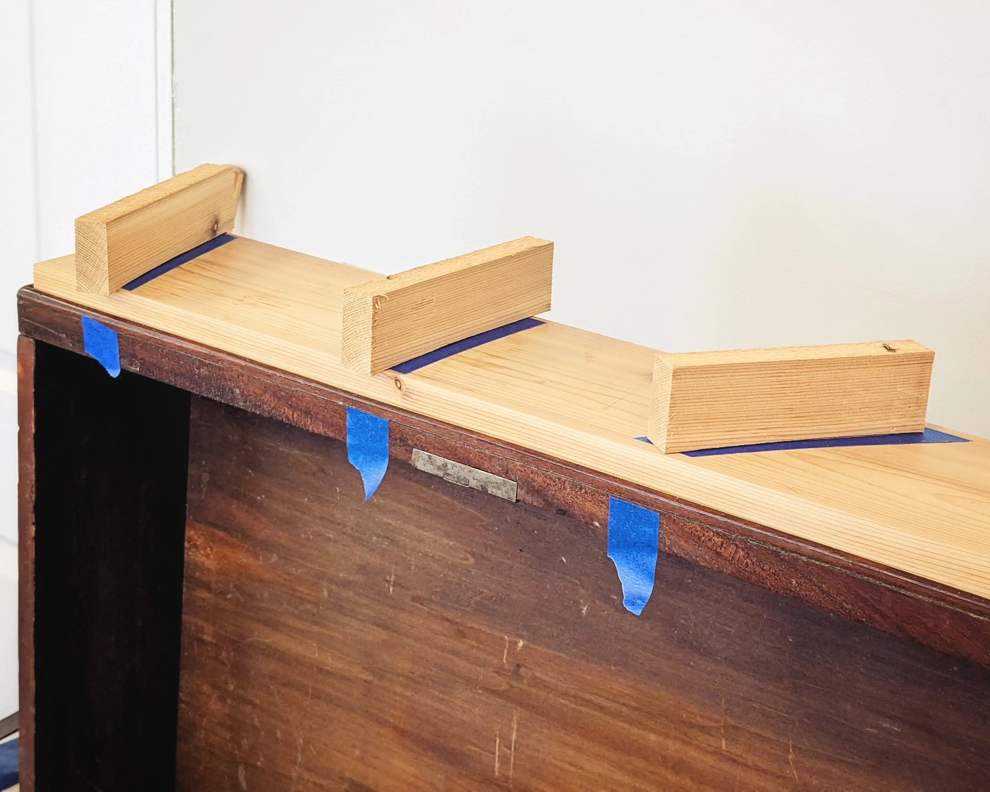 Probably nothing special for other restorer's out there, but thought I'd share a clamping tip for those who might find themselves in a similar scenario....
I'm gluing down some lifting veneer on this drawer front. There are three large areas that need the most attention and a bunch of very small areas dispersed across the drawer front. I'm going to tackle them all in one glue up using a large flat board across the drawer front (a sheet of parchment will go between the board and drawer front to prevent sticking).
The issue is I'll only have a rough idea on the location of the areas that need the most direct clamp pressure since I lack X-ray vision.
So I've marked the board with blue tape where I need the most pressure. Wooden cauls (seen here) will go right on top. And little pieces of blue tape on the drawer edge help register everything where it needs to be. Now I can get pressure where it's needed most and clamping the board down across the drawer front will take care of all the smaller repairs. Makes for one easy glue up!
#themoreyouknow🌠 #restoredinbaltimore