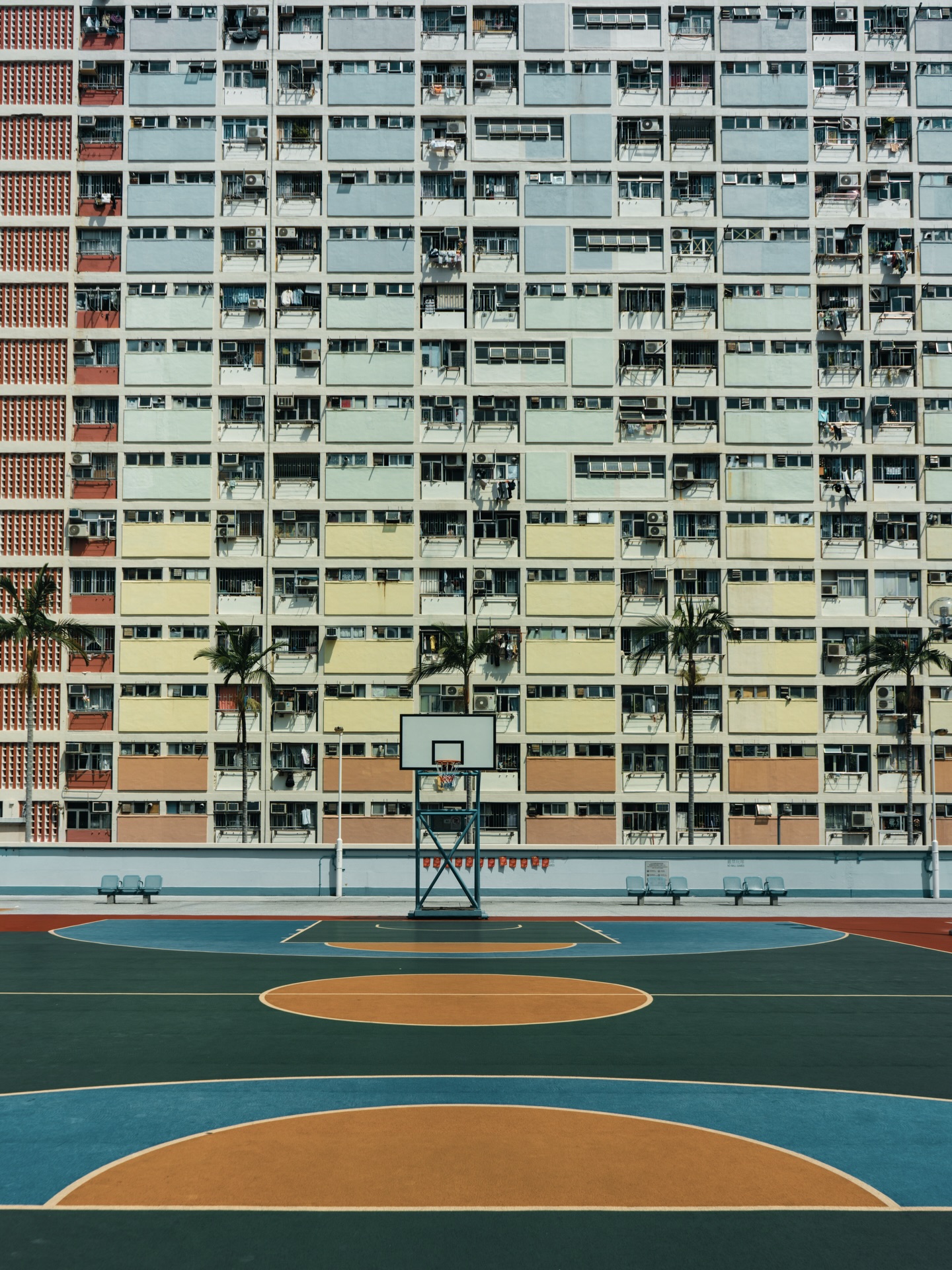 Mittag in Hong Kong. Die Sonne steht senkrecht über den Hochhäusern, die Luft flimmert zwischen Beton und Glas. Alles wirkt langsamer. Selbst der Verkehr scheint für einen Moment zu atmen.
Ich laufe durch enge Gassen, vorbei an Werkstätten, in denen sich Werkzeug, Kabel und Neonlichter stapeln. Ein alter Mann sitzt im Friseurstuhl direkt am Straßenrand, umgeben von Dingen, die Geschichten erzählen könnten. Nebenan klappert Metall, irgendwo summt ein Ventilator. Es riecht nach Asphalt, Staub und Mittagessen.
Ein paar Blocks weiter: ein Basketballfeld, eingerahmt von Wohnblöcken, die wie Raster in den Himmel wachsen. Hunderte Fenster, Klimaanlagen, Wäscheleinen. Struktur und Chaos gleichzeitig. Die Farben des Felds leuchten im harten Licht, Grün, Blau, Orange. Kein Schatten weit und breit. Nur Hitze, die vom Boden zurückstrahlt.
Dann wieder Stille in einem Innenhof. Zwei Frauen sitzen an einem kleinen Tisch, Karten in der Hand, konzentriert. Es sind diese kleinen Szenen, die bleiben. Nicht spektakulär, aber echt.
#HongKong
#StreetPhotography
#UrbanLife
#Asien
#Mittagshitze