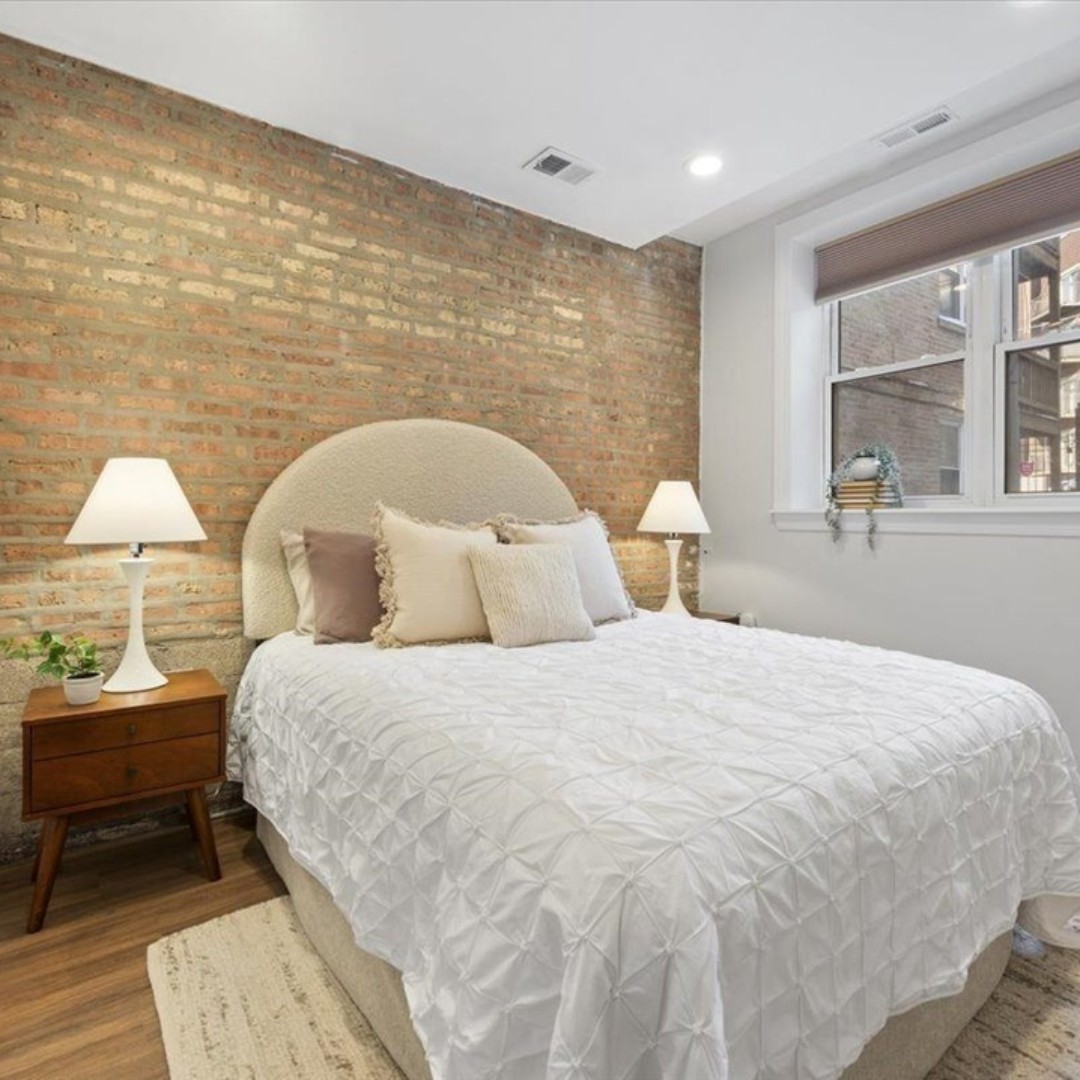 A sweet secondary bedroom moment — easy neutrals + curved silhouettes soften the brick accent wall to cozy up the room 😴 #neutrals #cozy #chicago #chicagorealestate #havenhomestager #chicagohomestaging #stagingworks #stagingsells #staging #homestaging