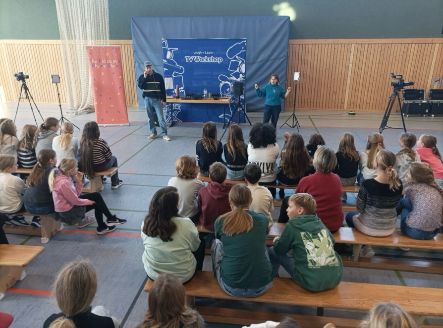 “Become TV-Star for a Day”
begeistert das CGG
– Workshop mit Laugh’n’Learn
Am 19.12.2025 wurde die Turnhalle des Christoph-Graupner-Gymnasiums Kirchberg
zur Bühne einer ganz besonderen Veranstaltung: Zwei professionelle Schauspieler der
Londoner Agentur Laugh’n’Learn waren am Christoph-Graupner-Gymnasium zu Gast
und brachten einen mitreißenden englischsprachigen Workshop mit.
Während der Durchgänge des TV-Workshops „Behind the Scenes“ schlüpften die
Teilnehmenden in ganz neue Rollen. Ob Produzent, Regisseur, FilmtechnikerIn,
MakenbildnerIn oder Schauspielerin bzw. Schauspieler– gemeinsam entwickelten die
Gruppen eine Stand-up-Filmszene, die sich augenzwinkernd an das bekannte Märchen
Cinderella“ anlehnte. Am Ende waren sich alle einig: Dieser Workshop war ein echtes
Highlight.
Dies verdanken wir auch unseren beiden Gästen, die mit Professionalität, Witz und
Herzlichkeit jede Menge Motivation und Freude in unsere Turnhalle gebracht haben.
Fortsetzung folgt!
Nach der gelungenen Veranstaltung des letzten Jahres freuen wir uns nun auf eine
Wiederholung der Zusammenarbeit mit Laugh’n‘Learn im Dezember 2026 - dann unter
dem Titel „AI Workshop“ und im angesagten TED-Talk-Format. See you soon!
#graupnergym #languagesarefun #languagelearning