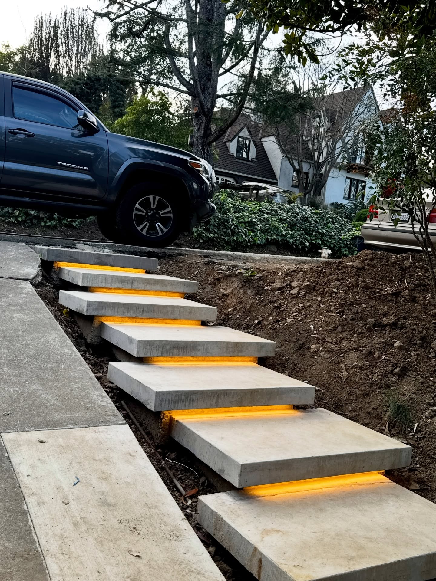 Modern hillside entry steps constructed with oversized concrete slab treads and integrated warm LED under-step lighting.
The design creates a floating effect, improves nighttime safety, and blends clean architectural lines with the natural slope of the landscape—functional, durable, and visually striking craftsmanship.