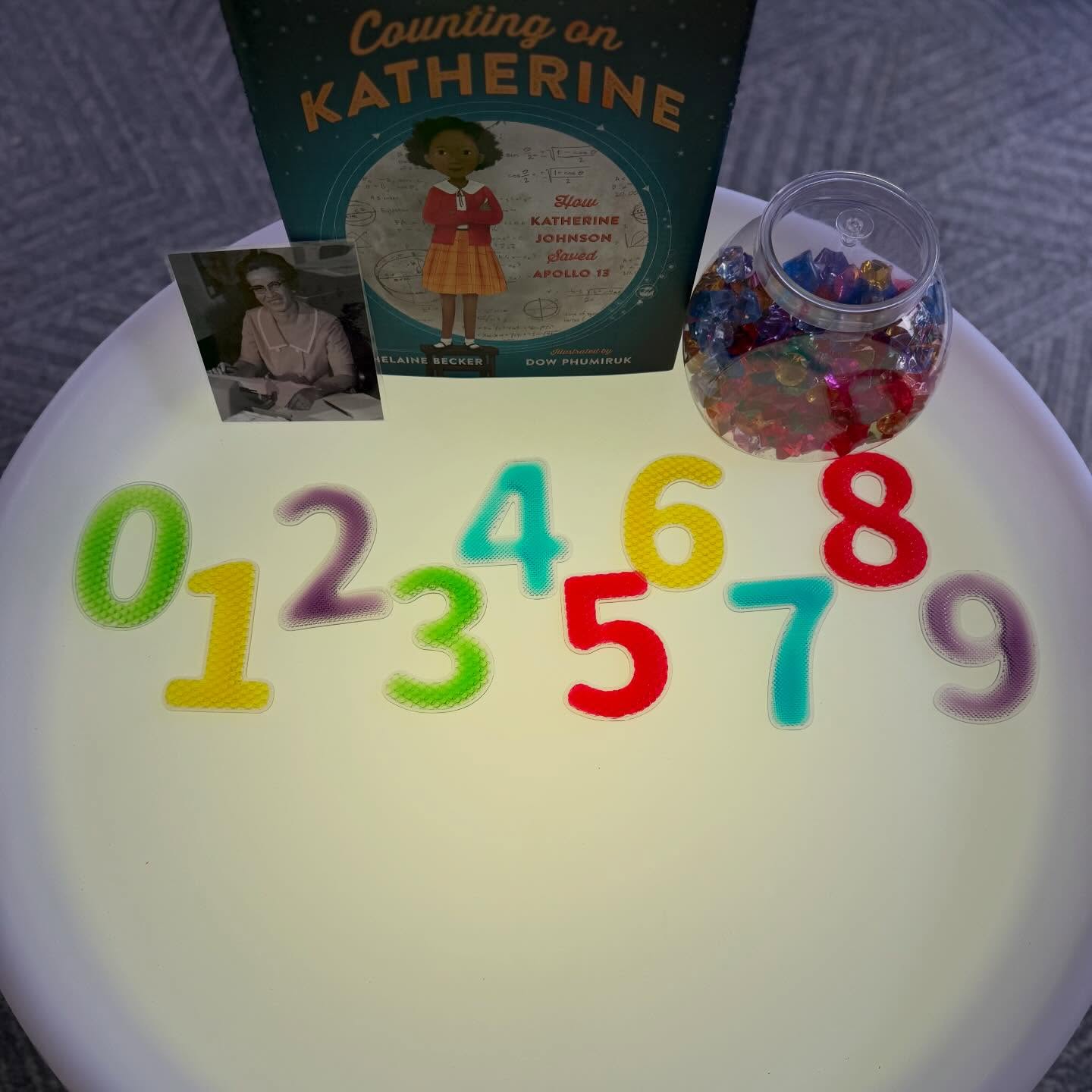 Inspiring Young Mathematicians Through Play for Black History Month //During #BlackHistoryMonth, learning about Katherine Johnson, an extraordinary mathematician whose love of numbers helped change history & send astronauts safely into space at NASA during a time when both women & Black Americans faced unfair barriers in science & education; her courage, determination, & brilliant thinking remind children that they can dream big & make a difference, & the book Counting on Katherine: How Katherine Johnson Saved Apollo 13 bringsher inspiring journey to life by sharing how she grew up, followed her passion for math, became a teacher, & later used her incredible skills to support historic space missions.
After reading the story to better understand her life, her impact, & why her story still matters today. This developmentally appropriate & engaging invitation was way a for children to explore numbers & one-to-one correspondence using loose parts. @discountschoolsupply sensory numbers & gems were placed out on the light table the children to explore, sort, & count as they played.
In the early years, children learn best when they can touch, move, & explore. Hands-on experiences help children make stronger connections between what they see and do, so they are building real understanding, not just memorizing numbers. This kind of playful learning helps make math feel familiar, comfortable, & enjoyable.
As children develop number sense, they move through 2 key stages of counting: rote counting & one-to-one correspondence. Rote counting is reciting numbers in order, while one-to-one correspondence is matching one number to one object. This 2nd stage is important because it helps children understand that numbers represent real amounts.
Open-ended, hands-on activities support this learning by helping children connect number symbols, spoken numbers, & real objects. As children count & place items, they build accuracy, focus, & confidence, & begin to see math as something they can explore & understand. #tinkerwonderplay #earlymathskills #loosepartsplay #lighttableplay