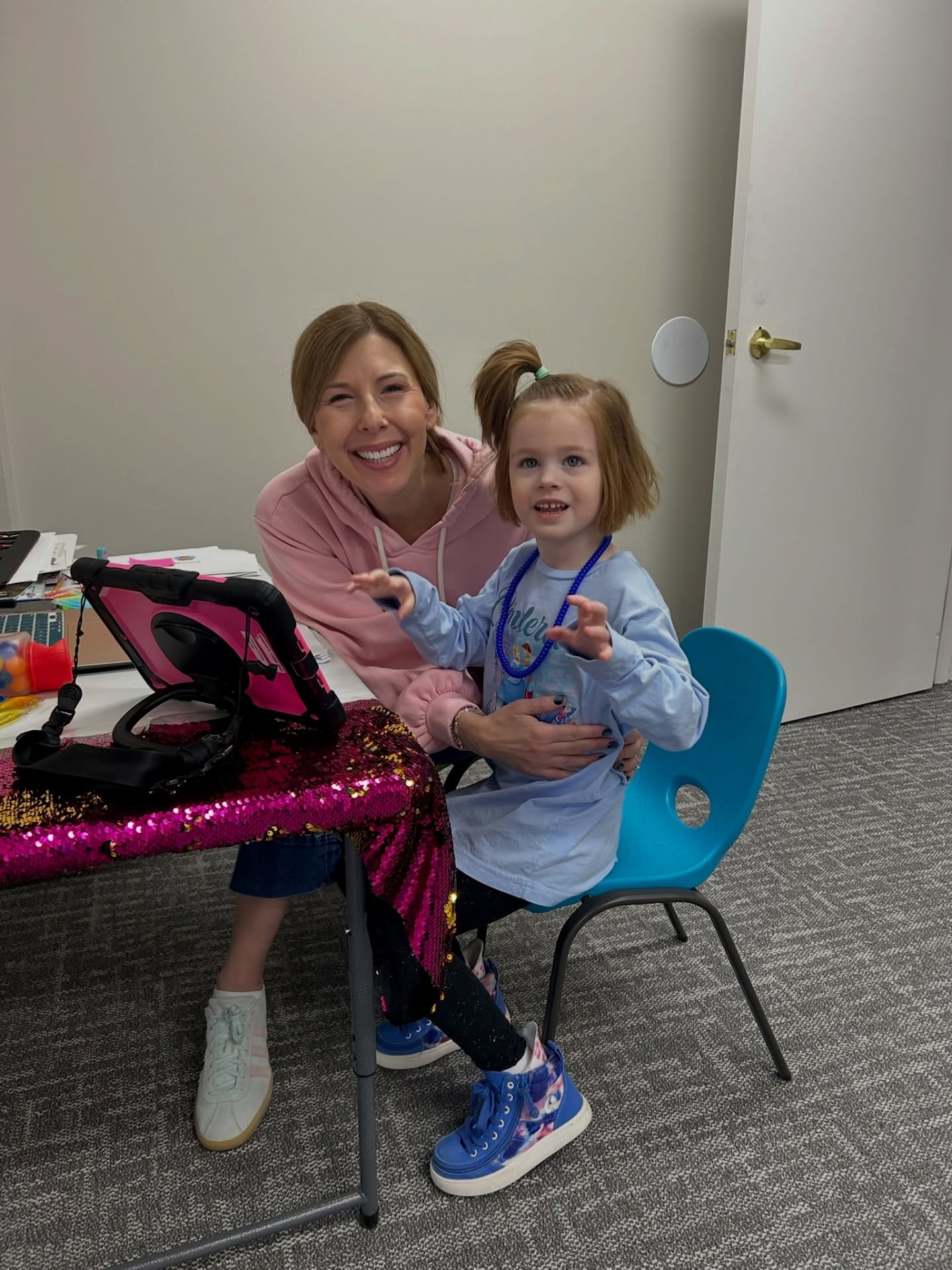 At REV, we prioritize connection over compliance. Before we ever work on skills, we work on trust. All our learners - like our littlest one here! - deserve a teacher who knows their favorite movie, celebrates their energy, and sees their full potential. From there, we build communication in ways that are student-led, joyful, and grounded in the belief that every learner is intelligent, capable, and has something meaningful to say. We presume competence, honor the brilliance each person brings, and hold high expectations because we know they are always learning.
#PresumeCompetence
#ConnectionOverCompliance
#CommunicationAccess
Image ID:
1: A woman in a pink hoodie sits at a sequined table smiling broadly, hugging a young girl with a ponytail and blue beaded necklace. An AAC tablet on a pink case sits on the table beside them.
2: A young girl in a lavender sweater reaches toward an AAC device on a pink case. Also visible are a laptop and a stencil alphabet board showing letters J through R.
3: A young girl leans forward focused on a laptop screen showing an animated scene, with an AAC device to her left and a picture card showing the word “Jam” and a stamp pad on the table in front of her.
4: A classroom wall with colorful circles in red, green, blue, purple, orange, and yellow, each labeled with a letter: P, H, C, S, T, and B. White tape lines divide the wall into sections, creating an interactive letter activity.