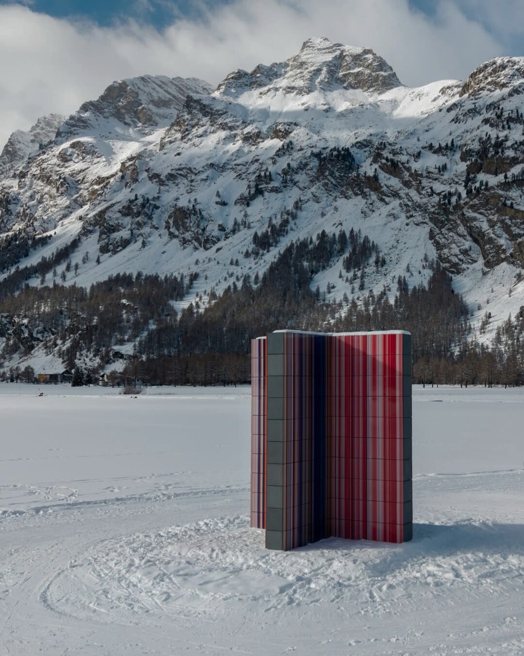 Dans le contexte alpin, toute intervention exige une précision absolue.
Strip Tower (962) est installée à Sils Maria, au bord du lac de Silvaplana, au cœur de l’Engadine. Le projet, porté par la Luma Foundation dans le cadre d’Elevation 1049, inscrit l’art contemporain directement dans le paysage.
Il ne s’agit pas d’une œuvre conçue pour un espace muséal fermé.
Elle est présentée en plein air.
Les visiteurs la découvrent dans la neige, le vent, la lumière changeante du lac. Ils la contournent, y pénètrent, deviennent partie intégrante de la composition.
D’un point de vue architectural, l’œuvre se lit comme une structure spatiale verticale :
— huit panneaux interconnectés
— un revêtement en carreaux de céramique aux bandes chromatiques
— un volume intérieur accessible
— la couleur comme élément constructif
La tour ne cherche ni à imiter le chalet alpin, ni à rivaliser avec la montagne.
Elle s’inscrit comme une géométrie pure dans l’horizontalité de la vallée.
La lumière en transforme la perception chaque jour :
le matin — une présence graphique et nette,
à midi — une vibration chromatique intense,
sous la neige — une abstraction presque silencieuse.
Pour GARON, cette installation illustre une idée essentielle : introduire une forme contemporaine dans un paysage naturel sans l’imposer, mais par la proportion, le rythme et le respect de l’échelle.
- Strip Tower (962)
- Sils Maria | Lake Silvaplana | 2026
- Présentée par Luma Foundation dans le cadre de Elevation 1049
- Visible jusqu’au printemps 2029
Image : @elevation1049