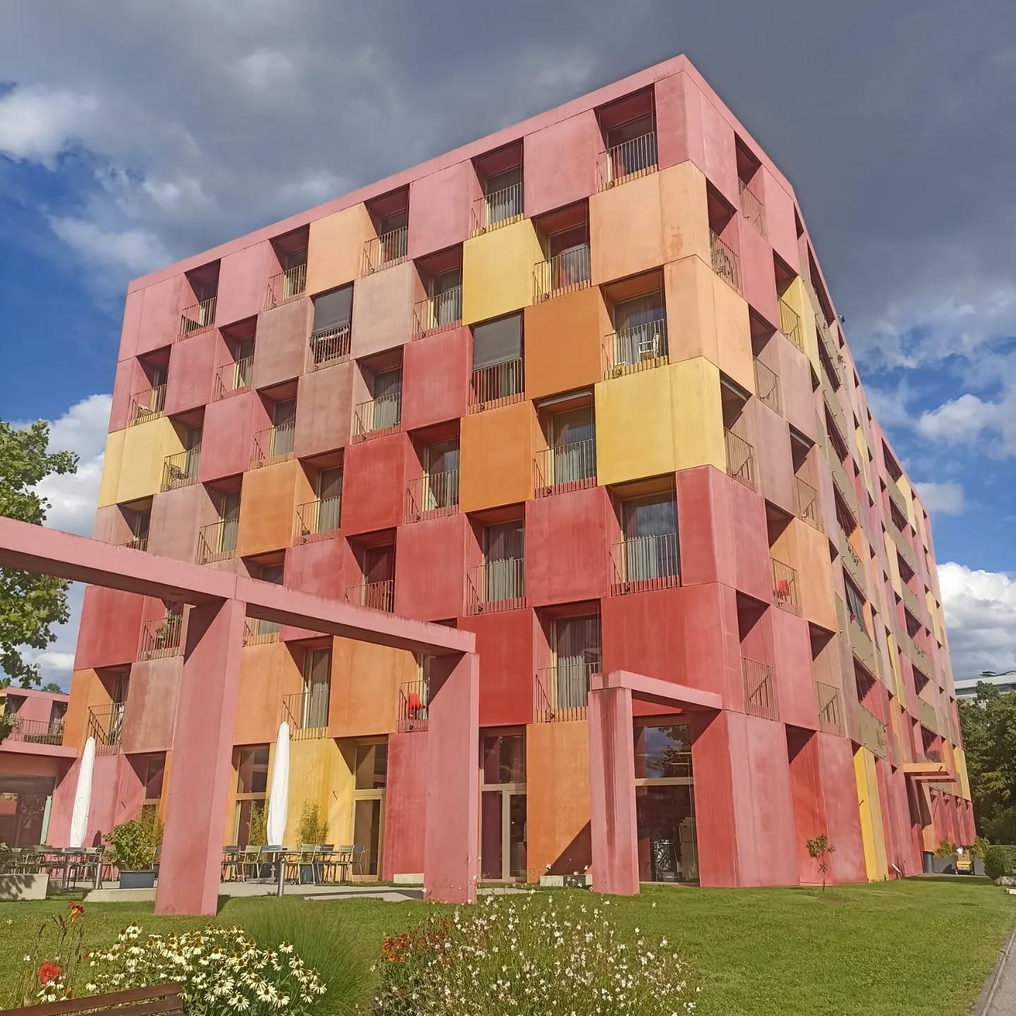 #designlabarchitecture #dlcarchitecture #emsnouveauprieure #lagradelle #lagradellegeneve #swissarchitecture #colorarchitecture
#colorfularchitecturefacade #suissearchitecture #architecturegeneve #genevaarchitecture #genevaarchitecturetour #guidingarchitectslausanne
# architecturaltour #visitesguidesgeneve #architecturegeneve
The “Nouveau Prieuré” complex is the first social experience in Geneva which contains an end-of-life residence combined with a day nursery and student housings.
To meet the requirements of this ambitious scheme, the project is based on the construction of three separate buildings surrounding a large circular square - in the form of a patio - around which flows a generous circulation area. The latter gives access to each of the communal parts of the scheme, such as the cafeteria, the administrative offices, the day nursery and the students’ living area, thus encouraging communication, mixing and social life.
The typology of the residential part for seniors adopts an architectural concept that is also original, with a principle of shared apartment in which eight people live together around a large living room. The quality of the dwelling is reinforced by the fact that the service spaces are placed at the back and by the natural light flowing in from a glass courtyard in the centre and laterally by a large south-facing loggia.
As regards the architectural design of the facades, these are in four different colours of precast concrete which catches the eye, and very slight inflexions of emerging volumes that allows perception to be enriched according to the standpoint. The general composition is embellished by the presence of closed gardens, the largest of which acts as the entrance.
Source: gvarchi.ch