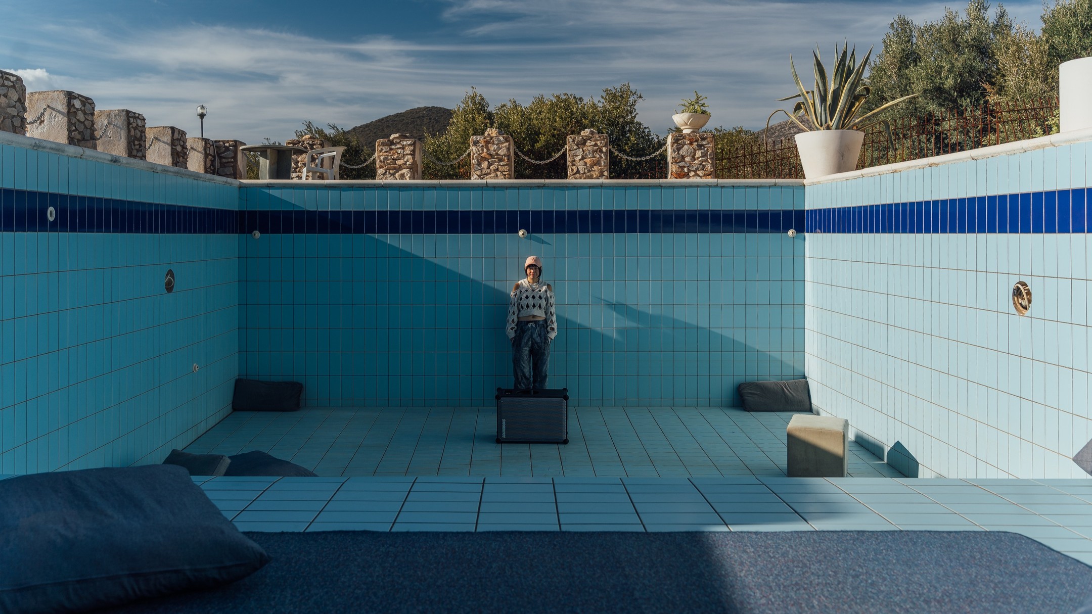 Chia-Liang Lai ( ether o ) is an interdisciplinary artist, drummer, producer, DJ, energy and sound practitioner from Taiwan, currently based in Berlin, Germany. Their diverse artistic portfolio encompasses sound, performance, music, video, radio and artistic research. Their performance practice has evolved into an ongoing exploration between body, movement, and sound, emphasizing themes of embodiment, care, and healing in the context of decolonial-eco-feminism. In their body-based practice, they often address social constructs impulsed to the bodies with sound and music, where listening and voicing are especially explored as political gestures and relational strategies.
In my work, I explore listening as a relational strategy within the contexts of decoloniality, ecology, and queer feminism. During the residency, I investigated local wildfires through field recordings at burnt sites, using the microphone as an extension—a tentacle into the ecology—arousing planetary sensitivity through the acoustic environment. Field recording here turns listening into a sonic gesture of care, a point of departure toward understanding and interconnectedness with nature.
The field recording materials portray the geography of Evia: the island’s windy conditions, a key factor in the acceleration of wildfires. In the sound production process, I translated the wind sounds into various rhythmic patterns that drive the composition, including shamanic drumming and the rhythm of breath, which points to breathing as a shared, collective act between humans and plants, whose respiration is an inverse yet interdependent process. The scale of breathing suggests our unity in the regenerative process. Based on the field recording material, I create binaural beats with different frequencies to generate healing sounds.
Sonic Incubator is a sound installation that transforms nature's soundscape into an immersive experience for collective restoration, highlighting sound as a bodily experience in the form of vibration.