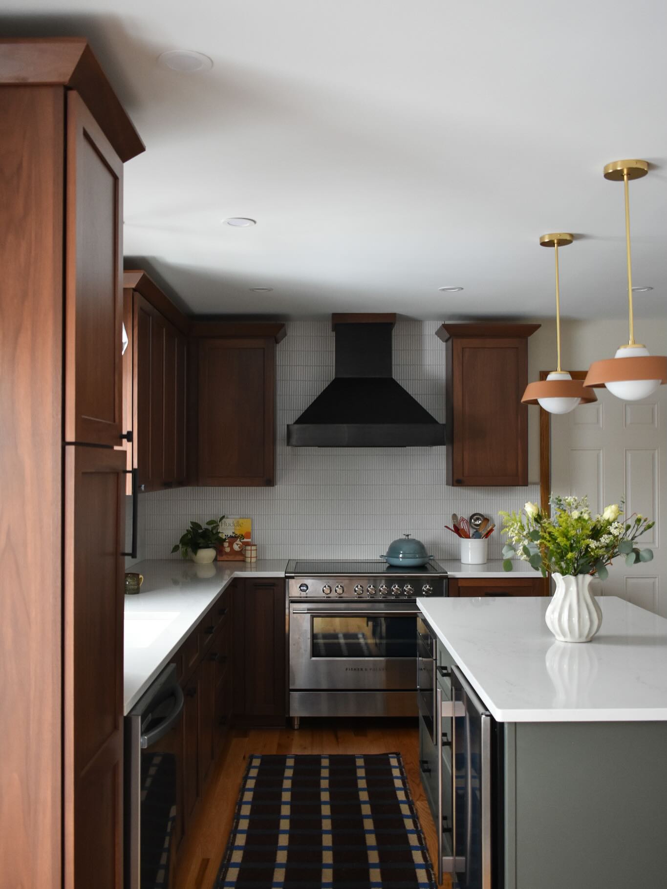 A kitchen transformation with pops of green and walnut cabinetry. In moving the range and fridge placement, we were able to broaden the working triangle in the kitchen. We removed soffit areas to extend cabinetry, and the floors were replaced with beautiful red oak. Check out the before photos at the end.