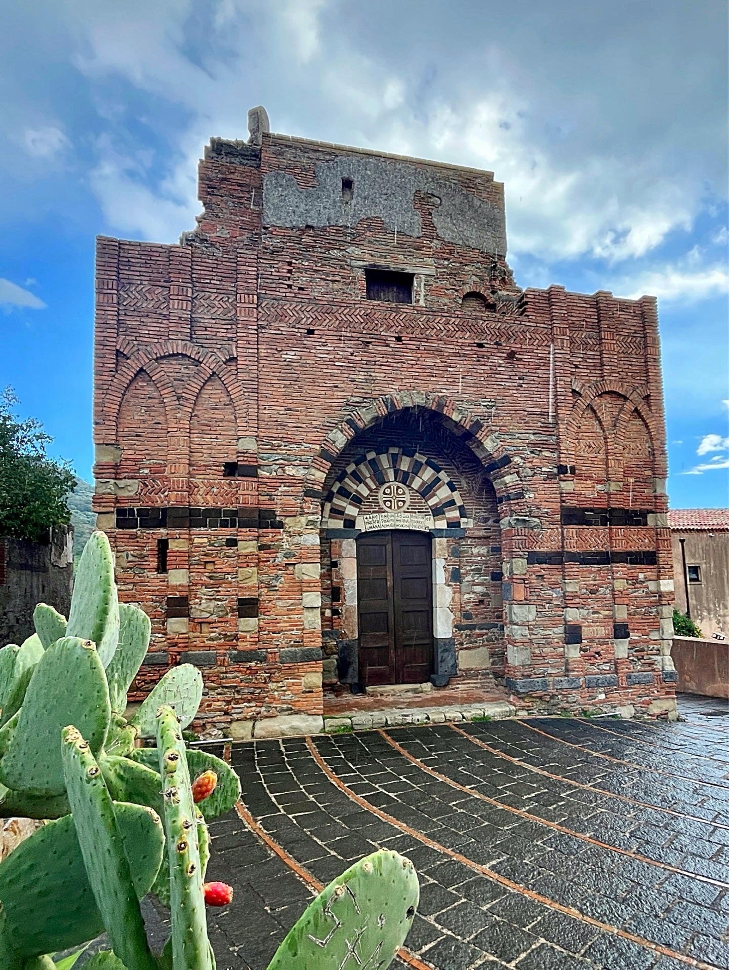 Im Jahr 1116 reitet der normannische König Roger II. von Messina nach Palermo, als ihn der Basilianermönch Gerasimo in Sant’Alessio anhält.
„Majestät, helft uns! Unser Kloster am Agrò-Fluss liegt seit den arabischen Kämpfen in Trümmern!“ Roger nickt und schenkt Land, Dörfer und Rechte für den Neubau der Kirche Santi Pietro e Paolo. Nur fünf Jahre später erhebt sich ein Meisterwerk, erbaut mit roten Ziegeln, schwarzer Lava und weißem Stein.
Fast vergessen steht das beeindruckende Bauwerk auch heute, 850 Jahr später, noch dort in Casalvecchio Siculo, ganz versteckt und nur über kleine Straßen und Wege zu erreichen.