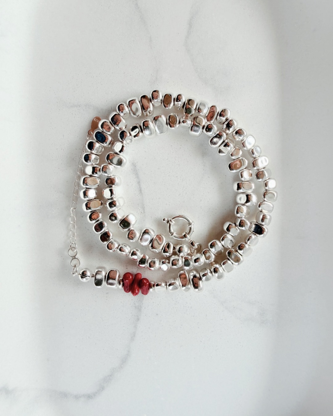ELEMENTS / POWER 01
Srebro w swojej najbardziej surowej i wyrazistej formie.
Miękkie, organiczne kształty koralików odbijają światło przy każdym ruchu, tworząc subtelną grę refleksów.
Centralnym akcentem jest czerwony koral – niewielki, ale pełen energii. Symbol siły, życia i odwagi.
To naszyjnik, który nie potrzebuje wielu dodatków.
Jest jak znak – prosty, mocny i charakterystyczny.