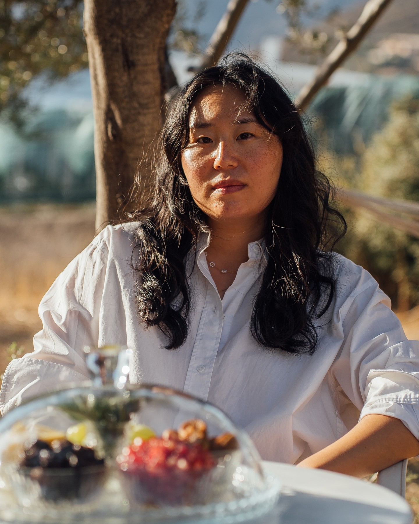 λεμόνι lemon ليمون citron
This sound-based work explores the connection between food, place, and memory. Though we may lose places in many ways—war, politics, climate change, migration, time—they live on in our stories. During a series of recorded interviews over local produce, participants narrate memories that resurface with each bite, transporting us to places frozen in time.
This project aims to map out memories of such places, and how they might be resurrected. How taste and place are connected. How grief and climate change intertwine. How, through all of this, memory becomes an indestructible force.
Throughout this residency, I conducted these interviews with locals restoring their lands in southern Evia through regenerative farming techniques. Over small bowls of local produce—lemon, prickly pear, pomegranate, rosemary, olives, and more—together we ate the foods one by one.
In these recorded sessions, we explore these memories in their mother tongues or languages of preference (Greek, Arabic, English, French). Memory comes from a deep place, and I wanted the most direct experience possible.
You are invited to rest in these hammocks or chairs, to gaze out at the sea and let the sounds of memory wash over you, to remember/resurrect your own lost places.
In this ongoing project, I am archiving place through memory and local tastes.
___________________
C. Grace Chang (Artist, Curator, Filmmaker)
C. Grace Chang (b. 1989, USA) is an artist, curator, and filmmaker based in Malmö. Born and raised in New Jersey, she is a Fourth Culture Kid and often explores liminality in her work. She combines decolonial theory with moving image, sound, and installation to examine the construction of visual safe havens, coded power structures, and refusal as a starting point.
While her works rely on theory, they are also rooted in grief, joy, and both collective and individual memory. Often using bright colors and fantastical elements in immersive installations, she explores futurity, care, and worlds beyond the colonial gaze.