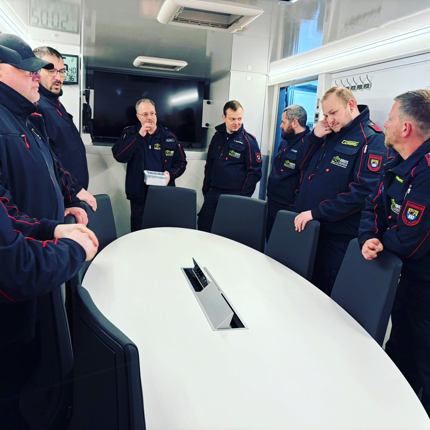 +++Übungsbericht+++
👉IuK-Einweisung auf den neuen „AB-Besprechung“.
Am Feuerschutztechnischen Zentrum des Kreises Düren steht ab sofort der neue Abrollbehälter „Besprechung“ (AB-Besprechung) als Einsatzmittel zur Verfügung. Der Abrollbehälter kann durch die kommunalen Feuerwehren angefordert werden und erweitert das Geräteportfolio der Informations- und Kommunikationseinheit (IuK) deutlich – sowohl im Standalone-Betrieb als auch in Kombination mit dem ELW3.
Gestern wurde die IuK-Mannschaft intensiv mit dem neuen System vertraut gemacht. Der AB-Besprechung bietet im Vergleich zum Vorgängermodell eine deutlich erweiterte Funktionalität. Dazu zählen unter anderem eine autarke Notstromversorgung, eine eigene Netzwerkinfrastruktur mit Internteanbindung und WLAN sowie ein integriertes Monitorsystem zur Lagedarstellung. Darüber hinaus ist eine direkte Konnektivität zum ELW3 oder Drohnen MZF gewährleistet, wodurch sich der Abrollbehälter optimal in bestehende technische Infrastruktur einfügt.
Neben der einsatztaktischen Ausstattung verfügt der AB-Besprechung auch über verschiedene Komfortmerkmale, die insbesondere bei längeren Einsatzlagen von Vorteil sind. Hierzu zählen eine fest installierte Kaffeemaschine, Kühlmöglichkeiten sowie eine Mikrowelle.
Im Rahmen der Einweisung konnten sich die Einsatzkräfte ein umfassendes Bild von den neuen Möglichkeiten machen und die Handhabung praxisnah erproben. (pb)