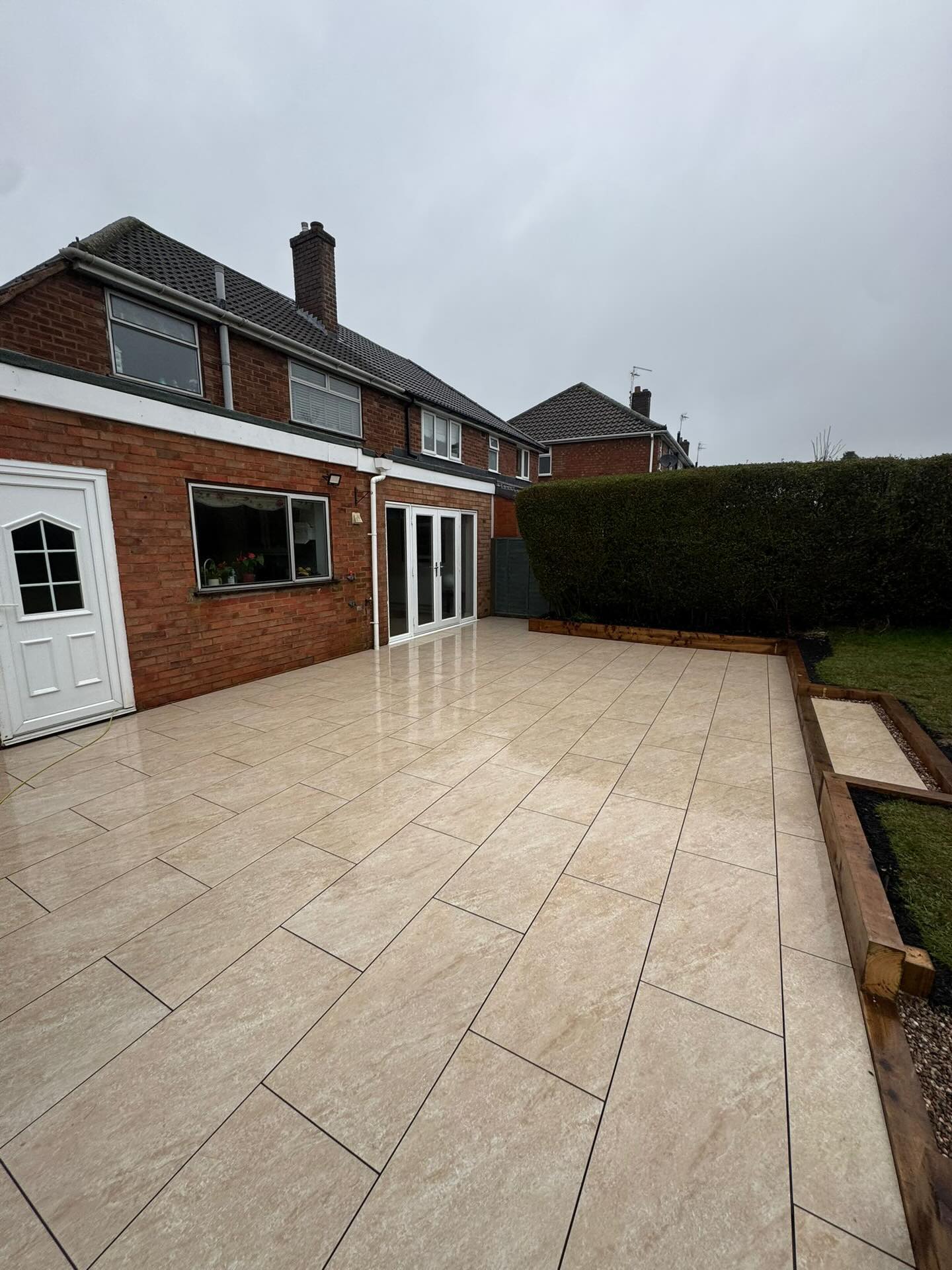 There’s a detail in this project that we’re particularly proud of. The clients had always had to step down from their back door into the garden — a small thing, perhaps, but one that quietly shapes how you experience your outdoor space every single day.
Using a suspended porcelain paving system, we were able to raise the finished level flush with the threshold, transforming what had been a fragmented, multi-level patio into one generous, connected terrace. The tile is a warm beige stone effect porcelain — understated, timeless, and just the right side of luxurious