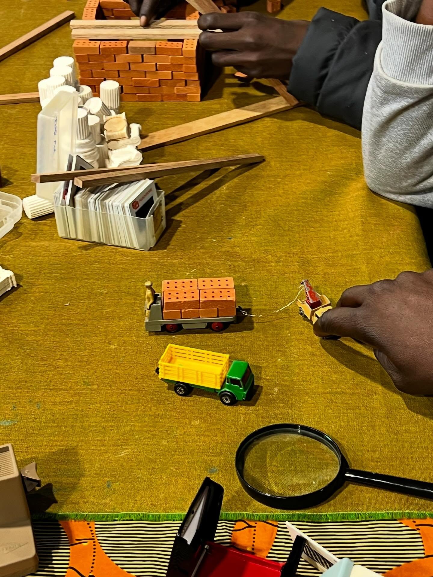 POSSIBILITIES TO PLAY
Calais, March 25th 2026
It was changeable late March weather - hail, some sunshine, dark grey skies, and finally a rainbow.
To ground our selves back in Calais we visited several of the informal living sites, as well as the fields of large rocks placed to deter people displaced in the city from settling for the night. We noticed how the landscape has changed once again.
This afternoon in the day centre @calais.exilessc The Community Table was used to the full. In discussion with the coordination team we were located in a new position in the main space. Collectively we activated the table by first using the materials ourselves. Knowing to trust the process, more than 40 teenage boys and men slowly found their way to the table, enjoying the crisp detail in the slides through the retro viewers, carefully constructing miniature buildings and little home scenes, lining up and revving up the toy trucks - everyone sitting side by side around the table. It was heartwarming to see how engaged people were in play.
The day centre itself was very busy, with the vast majority of people using it from Sudan, with high numbers of young unaccompanied teenage boys.
Although Sudan is little in the news, it is now the largest displacement crisis in the world: around 5 million children have been forced from their homes while 17 million are requiring humanitarian assistance (ref: @savechildrenuk).
Tomorrow we return to our fortnightly online psychosocial support group for the staff team @greenkordofan in Yida Refugee camp in South Sudan. There, in spite of immense challenges, over 1000 children are supported through sports, personal development and the fundamental and hopeful possibilitIes to play.
Bobby Lloyd, Miriam Usiskin
#sudan #displacement #thecommunitytable