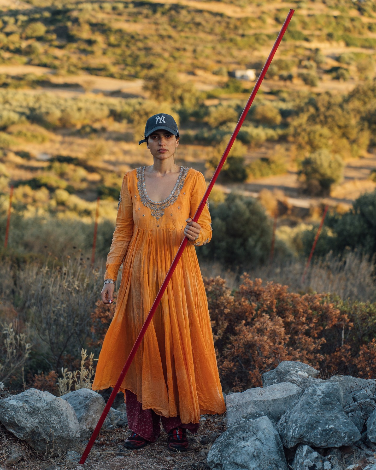 Anoēton , Unconceived
A hillside emergence influenced by Parmenides’ poem, On Nature, describing his way into the underworld. A consideration of near death, the ancient rites of Apollo, and the day of a shepherd. The pieces are made from the gleaning and reformulating of abandoned elements from Styra in rural Evia, Greece.
“Pulling the chariot at full stretch”
A downhill path leads to twin columns
At the gate: metal twisted into a digital ‘8’
Lemniscate – Rebar, tire, and burnt wood
“The sound the chariot makes as the daughters of the sun draw him along, the sound of a pipe (syrinx)”
Syrinx – 12 red telescopic poles
Thin red lines
Lines of red in the wildflowers
Conduct me to an abandoned mill
“In the middle of these is the divinity (daimōn) who steers everything“
Daimōn
– Rebar, metal coil, wax, PVC floating fish, persimmon, acrylic nails
Stela Xhiku Born 1990 Tirana, Based in New York.
Stela believes in a solar-powered future. A recent graduate of NYU's Interactive Telecommunications Program (ITP), she spent three years developing a robotic mirror, or Heliostat. A lifetime of rescuing litter has given Stela an abundance of materials, inspiring an improvisational art practice that is also an archaeological and spiritual study of modern waste.