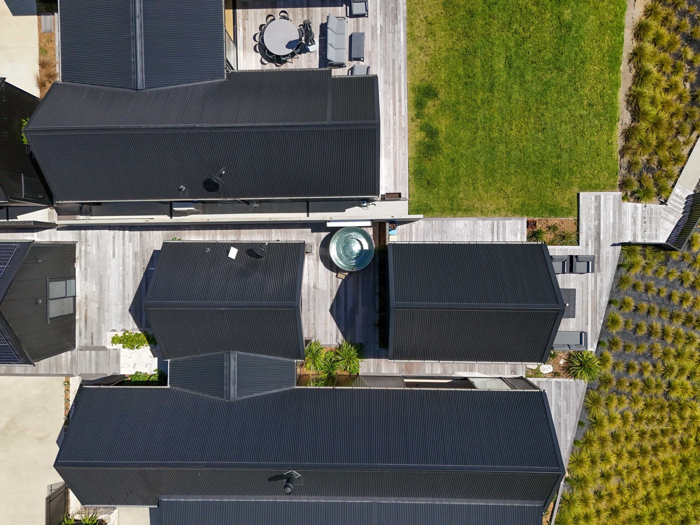 Side by side, the two dwellings form a quiet cluster — a refined nod to traditional lakeside sheds, reimagined through a distinctly architectural lens.
From above, the inspiration is clear. Drawing on the simplicity of an old corrugated iron boat shed, the homes are expressed through strong 40-degree gable forms that cascade down, anchoring each structure into the landscape.
Designed to sit gently within their surroundings, the dark iron-clad exteriors recede into the native hillside, allowing the architecture and environment to exist in balance.
Sustainability was considered at every stage — with a full solar system installed, and a thoughtful approach to water management. Stormwater is carefully recycled and filtered, returning back into the home’s domestic system after discharge to the lake.