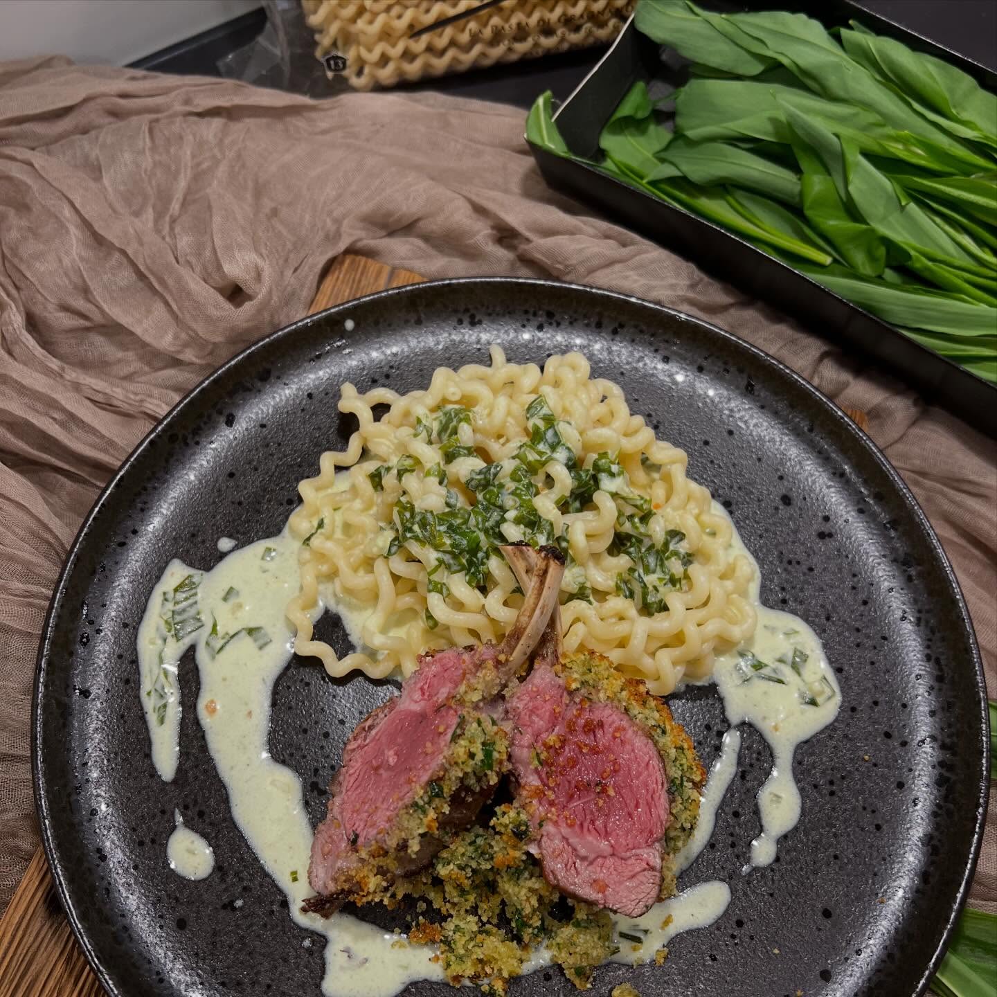 Lammrack mit Bärlauch-Kruste, Nudeln & Bärlauchsauce
Zartes Lammfleisch, aromatischer Bärlauch und eine cremige Sauce – dieses Gericht bringt den Frühling direkt auf den Teller.
Das saftige Lammrack wird mit einer knusprigen Bärlauch-Parmesanhaube überbacken und erhält dadurch ein intensives, würziges Aroma.
Elegantes Gericht, das sich ideal für ein besonderes Dinner an Ostern eignet und dennoch mit etwas Vorbereitung einfach zuhause zubereitet werden kann.
Zutaten für 2-3 Personen:
1 Lammrack (ca. 500-600 g)
Salz & Pfeffer
Bärlauch-Kruste:
1 EL Butter, weich
1 Knoblauchzehe, gehackt
1 Handvoll Bärlauch, gehackt
60 g Paniermehl
20 g Parmesan
Salz & Pfeffer
Bärlauchsauce:
1 EL Butter
1 Zwiebel, gehackt
1 dl Weisswein
2 dl Rahm
1 Bund Bärlauch, in feine Streifen geschnitten
Salz & Pfeffer
200-250 g Garofalo Fusilli Lunghi, al dente gekocht
Zubereitung:
Für die Kruste alle Zutaten vermengen und mit Salz & Pfeffer würzen, beiseite stellen.
Den Backofen auf 250°C Ober-/Unterhitze vorheizen.
Für die Sauce die Butter in einer Pfanne erhitzen und die fein gehackte Zwiebel darin glasig dünsten.
Mit Weisswein ablöschen und kurz einkochen lassen.
Den Rahm dazugeben und 5 Minuten leicht köcheln lassen.
Dann den fein geschnittenen Bärlauch hinzugeben und mit Salz und Pfeffer abschmecken.
In einer Pfanne etwas Olivenöl erhitzen und das Lammrack rundherum 3-4 Minuten kräftig anbraten. In eine Gratinform legen und rundherum mit Salz und Pfeffer würzen.
Die Bärlauch-Parmesan-Paniermehlmischung auf der oberen Seite des Lammracks verteilen und leicht andrücken.
Für ca. 10 Minuten im Ofen goldbraun gratinieren, herausnehmen - in Koteletts schneiden und mit den al dente gekochten Nudeln und der Sauce anrichten .
En Guete!