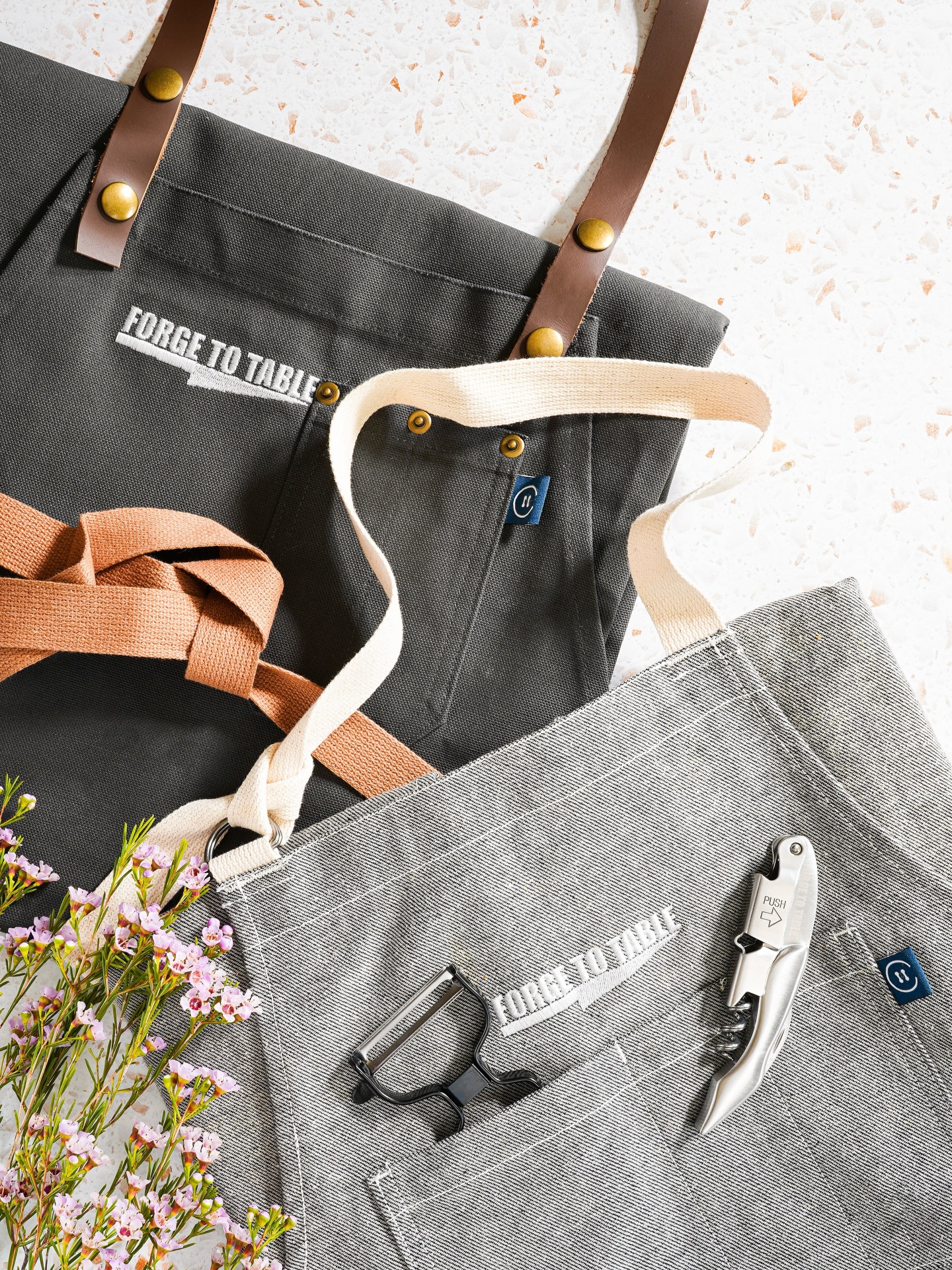 If you weren’t aware… we have aprons!
Since the beginning, Forge To Table has been dedicated to empowering culinarians of all levels with top-notch knives and accessories. That same dedication extends to our kitchen apparel, brought to life through our partnership with @caysondesigns to create our durable, beautifully made aprons.
We offer three styles to choose from, perfect as a gift on their own or paired with a blade!