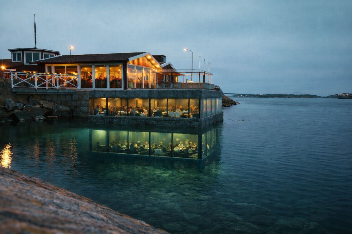Restaurang Tullhuset utvecklas med en ny tillbyggnad som förstärker kopplingen till havet. Projektet utformas i natursten och glas, förankrat i havsbotten, och skapar två tydliga nivåer – en i höjd med kajen och en under vattenytan.
Den övre delen erbjuder öppna vyer över skärgården, medan den nedre ger en unik, omslutande upplevelse av det marina livet genom stora glaspartier med fin indelning. Ljusets filtrering genom vattnet bidrar till en särskild atmosfär.
Tillbyggnaden tillför cirka 100 nya sittplatser och skapar en sammanhängande sekvens från landskap till undervattensmiljö, där arkitektur, gastronomi och natur samverkar.
