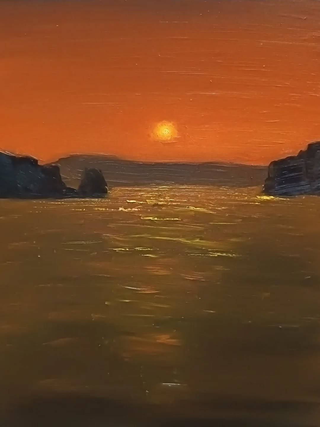 L'Architettura dell'Emozione: La Struttura Visiva
Da un punto di vista puramente tecnico, la composizione è rigorosa. C'è un orizzonte alto e una "cornice naturale" formata dalle rocce scure ai lati.
La corrispondenza emotiva: Questa struttura non è casuale. Le scogliere scure e massicce ai lati funzionano come un sipario teatrale o, meglio ancora, come i paraocchi della nostra attenzione. Ci impediscono di guardare altrove e ci forzano a focalizzarci sul centro luminoso. Emotivamente, questo crea un senso di concentrazione profonda e di soggezione. Lo spettatore si sente piccolo di fronte all'immensità che si svela tra le rocce, come se stesse assistendo a un segreto della natura. L'orizzonte alto sposta l'enfasi sull'acqua e sui suoi riflessi, accentuando la sensazione di essere "immersi" nella scena piuttosto che semplici osservatori distanti.
La Vibrazione del Colore: Temperatura ed Energia
La tavolozza è ristretta ma estremamente potente, basata su un contrasto termico netto.
Cielo Arancione Intenso:
* Tecnica: Una stesura piatta e orizzontale di un arancione saturo, quasi puro.
* Emozione: È un colore che irradia calore fisico. Non è un tramonto tenue, è un momento di intensità passionale e drammatica. Comunica una quiete che non è stanchezza, ma una pausa densa di energia prima della notte. C'è qualcosa di primordiale in questo colore, che evoca il fuoco e la vita.
Riflessi Dorati e Acqua Bruna:
* Tecnica: L'uso geniale di toni ocra-gialli e bruni (come Terra d'Ombra e Giallo Cadmio) che creano una scala cromatica degradante. Il riflesso solare è ottenuto con un'applicazione di pigmento denso e materico.
* Emozione: L'acqua bruna e scura in primo piano dà un senso di mistero e profondità ignota, ma il riflesso dorato e denso che la attraversa funziona come un sentiero di speranza e connessione. Quella luce "solida" invita metaforicamente a camminarci sopra. È una luce calda e accogliente, che contrasta con la "freddezza" della forma scura delle rocce.
La Materia e la Pennellata: Il Tocco dell'Uomo
La texture del dipinto è cruciale. Non è una superficie liscia.
Pennellate Orizzontali ed Effetto Impasto:
* Tecnica: Le pennellate orizzontali sono ovunqu