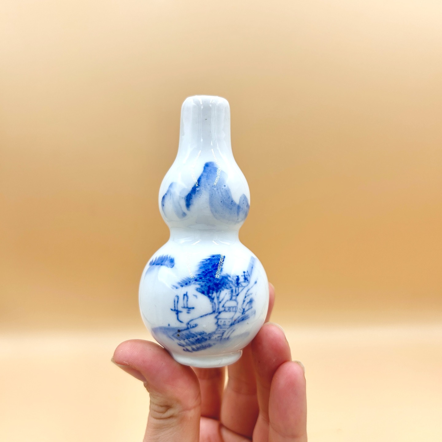 🟢 DOSTĘPNY | Maleńki wazonik qinghua, Chiny, Jingdezhen, lata 50 XX w.
Niewielkiej postury, ale wielkiego uroku wazonik qinghua/white-blue w popularnym kształcie tykwy/double gourd (hulu).
Forma tykwy, o wyraźnie zaznaczonych dwóch kulistych segmentach i zwężonej szyjce, ma silne konotacje symboliczne w kulturze chińskiej — utożsamiana jest z długowiecznością, ochroną i pomyślnością.
Dekorację wazoniku stanowi swobodnie malowany pejzaż w stylu literackim (wenren hua), przedstawiający górzysty krajobraz z drzewem, architekturą pawilonową i postaciami, operujący rozmyciami kobaltu i zróżnicowaną intensywnością pigmentu, co sugeruje szybkie, szkicowe pociągnięcia pędzla. Górna partia naczynia zdobiona jest uproszczonym motywem gór, co kompozycyjnie równoważy scenę figuratywną na brzuścu.
Wys. 10 cm
65 PLN + 15 PLN koszt wysyłki