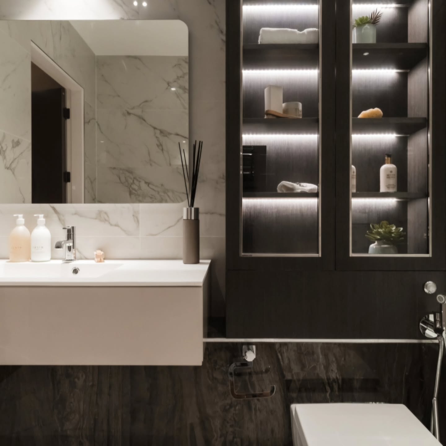 This recent project was all about balancing bold contrast with functional luxury. By pairing deep, charcoal marble against crisp white stone, we created a space that feels both grounded and airy.
Dark textured lower walls set against bright, veined marble tiles.
Custom cabinetry featuring integrated LED shelving for a soft, ambient mood.
A minimalist floating basin that keeps the floor plan open and clean.
High-end chrome fixtures and glass partitions for a seamless, spa-like flow.
A perfect example of how thoughtful lighting and texture can transform a standard bathroom into a high-end retreat.