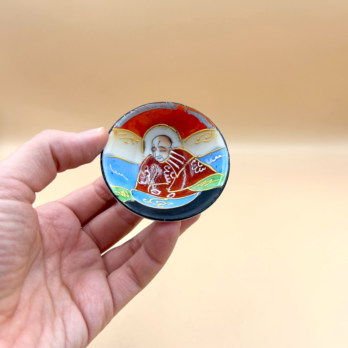 🟢 DOSTĘPNA | Czareczka z arhatem, Japonia, lata 40-50. XX w.
Czarka do gongfu/sake w stylu mid-century satsuma revival, którą charakteryzuje swoboda lini i mocne kolory. Stan idealny minus - lekkie starcia emalii na rancie.
Satsuma revival odnosi się do odrodzenia i reinterpretacji stylu ceramiki satsuma w Japonii pod koniec XIX i na początku XX wieku, szczególnie w kontekście produkcji eksportowej po okresie Meiji. W tym czasie warsztaty zaczęły masowo wytwarzać wyroby o charakterystycznej, bogato zdobionej powierzchni z użyciem złocenia i drobnych, precyzyjnych dekoracji figuralnych oraz ornamentalnych. Revival ten miał w dużej mierze charakter komercyjny i odpowiadał na zachodni popyt na „egzotyczną” estetykę Japonii, co wiązało się z pewną standaryzacją i stylizacją motywów.
W latach 50.–60. XX wieku nastąpiła kolejna faza tzw. Satsuma revival, tym razem silnie związana z powojenną produkcją eksportową, zwłaszcza na rynek amerykański. Wyroby z tego okresu cechują się uproszczoną techniką, często z użyciem kalkomanii i mniej precyzyjnego złocenia, przy jednoczesnym zachowaniu charakterystycznej, „gęstej” ornamentyki i ikonografii (sceny dworskie, gejsze, motywy figuralne).
Poj. 40 ml
70 PLN + 15 PLN koszt wysyłki