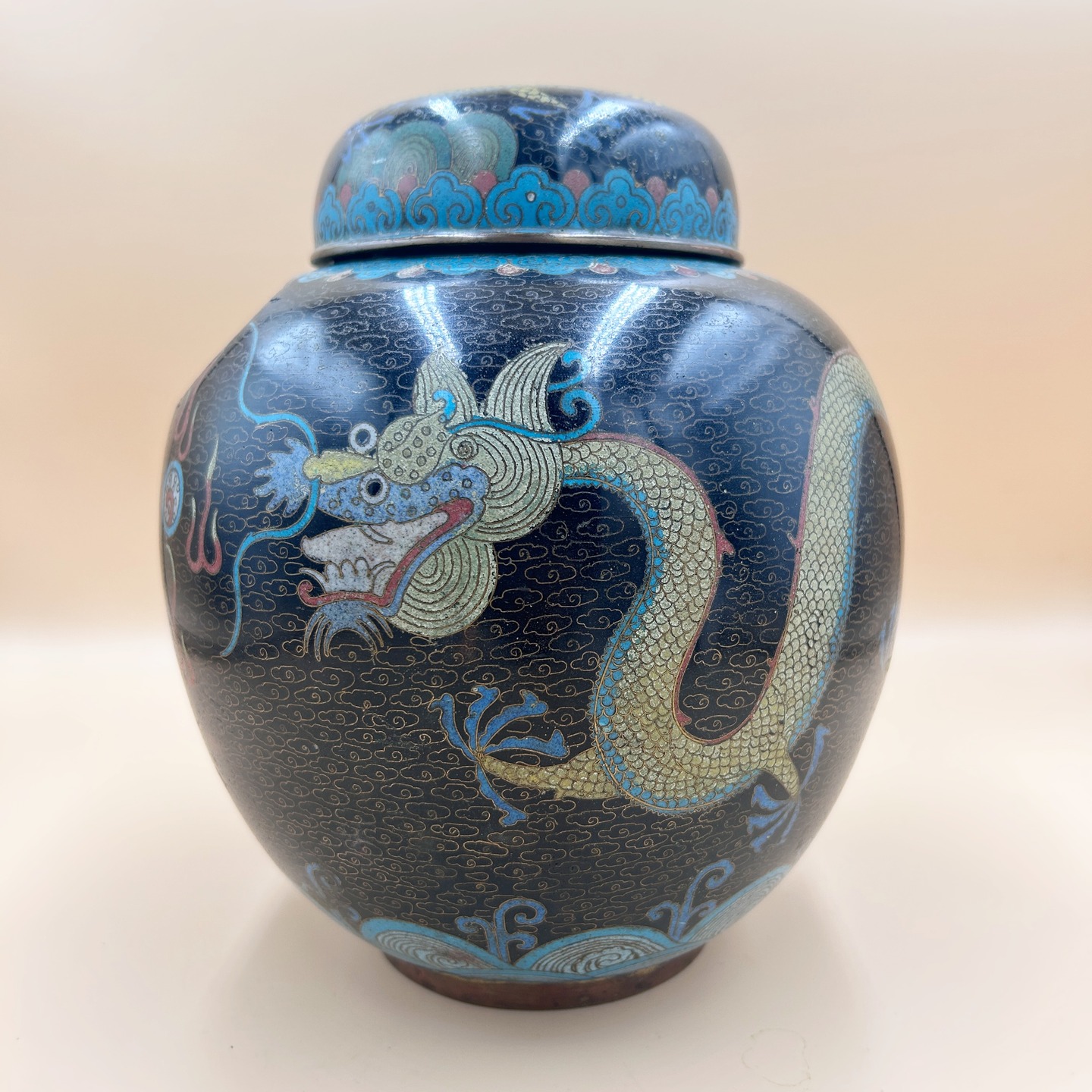 🟢 DOSTĘPNY | Ginger jar ze smokami cloisonne, Chiny, lata 1930-40.
Zjawiskowy, duży ginger jar ze smokami goniącymi perłę.
Motyw smoka (龙, lóng) należy do najważniejszych symboli w kulturze chińskiej i jest tradycyjnie związany z władzą cesarską, siłą oraz kosmicznym porządkiem. Pięciopazurzasty smok był zarezerwowany dla cesarza i oznaczał najwyższą rangę, a jego obecność na przedmiotach podkreślała prestiż oraz aspiracje do autorytetu i pomyślności.
Perła, często przedstawiana jako tzw. „płonąca perła” (火珠, huǒzhū), jest kluczowym atrybutem smoka i symbolizuje mądrość, duchową energię oraz spełnienie pragnień. Smok dążący do perły lub ją chwytający interpretuje się jako obraz poszukiwania wiedzy i kosmicznej prawdy, a także jako znak potęgi kontrolującej siły natury.
Towarzyszące mu stylizowane chmury (yunwen) symbolizują sferę niebiańską oraz dynamiczny ruch energii qi, w której smok się porusza, pełniąc rolę władcy żywiołów – zwłaszcza wody i deszczu.
Kompozycja jako całość ma charakter apotropaiczny i życzeniowy, wyrażając ochronę, dobrobyt oraz harmonię między niebem a ziemią.
Ginger jar na dwa uszkodzenia. Stan oceniamy na bardzo dobry minus ze względu na jakość wykonania ginger jaru.
Wys. 25 cm
Szerokość 28 cm
250 USD/ 700 PLN + 20 PLN koszt wysyłki