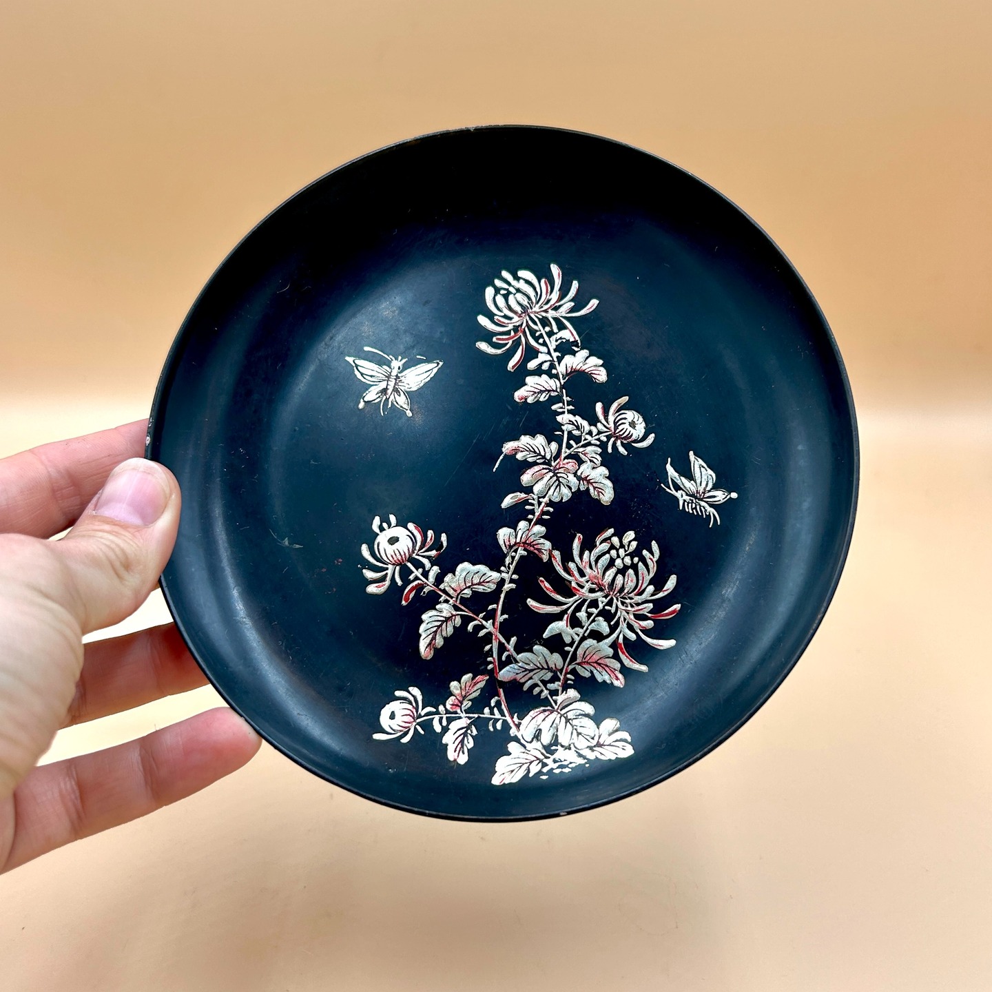 🟢 DOSTĘPNY | Talerz z chryzantemami, Japonia, lata 70-80. XX w.
Japoński talerzyk wykonany w technice imitacji laki urushi z motywem chryzantem i motylem z emalii opruszonej srebrnym proszkiem.
Motyw chryzantemy (kiku) w sztuce japońskiej jest silnie związany z ideą długowieczności, odnowy oraz symboliką cesarską, stanowiąc emblemat rodu panującego. Motyle natomiast odnoszą się do ulotności życia, przemiany i piękna chwili, często pojawiając się w kontekście estetyki efemeryczności (mono no aware). Zestawienie chryzantem i motyli tworzy poetycki obraz natury, łączący trwałość z przemijaniem, co jest charakterystyczne dla japońskiej wrażliwości.
Stan dobry - talerzyk nosi typowe dla starszej laki otarcia, ale nie widać ich z daleka (trzeba się na prawdę przyjrzeć). To talerzyka dołączamy zawieszkę na ścianę za dodatkowe 10 PLN.
Śr. 16 cm
35 PLN + 10 PLN stelarz na ścianę + 15 PLN koszt wysyłki