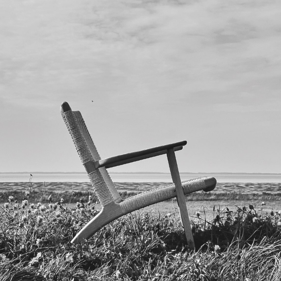 Der findes steder, hvor linjerne bliver enklere,
og hvor verden næsten falder til ro af sig selv.
Her står CH25 – tegnet af Hans J. Wegner i 1949 –
ikke som et møbel, men som en tanke i form.
Flettet i hånden, lag for lag, med en tålmodighed
der næsten kan mærkes i stilheden omkring den.
Træet bærer kroppen.
Papirgarnet bærer tiden.
Midt i landskabet, hvor horisonten er åben,
giver stolen plads til det, vi ofte glemmer –
at sidde, at se, at være.
Intet er overflødigt.
Intet råber.
Kun en stille præcision,
der stadig taler –
mere end 75 år senere.
#HansJWegner #CH25 #CarlHansenOgSøn #DanskDesign #Møbelklassiker DesignMedHistorie SkandinaviskDesign TidløstDesign Håndværk Æstetik Ro Marsken