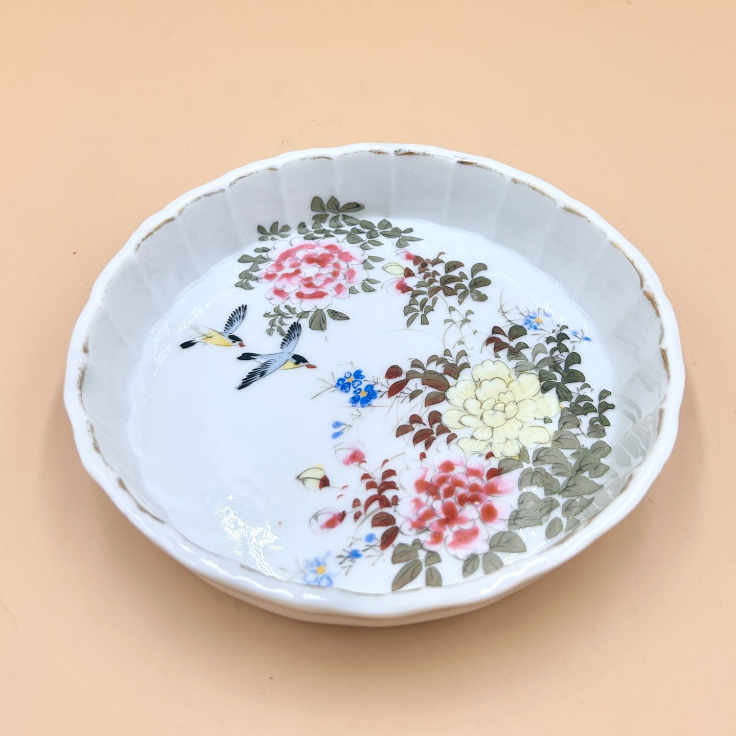 🟢 DOSTĘPNY | RZADKOŚĆ!! Talerzyk seto-yaki, Japonia, pocz. XX w., okres Meiji
Niewielki talerzyk wykonany w tradycji Seto-yaki, przypisywany warsztatowi Katō Shunkō (加藤春光), reprezentuje charakterystyczne dla XX-wiecznej ceramiki japońskiej połączenie subtelnej elegancji z użytkowym minimalizmem.
Forma o lekko falującym, modelowanym brzegu (tzw. rin-ka) została pokryta jasnym, mlecznobiałym szkliwem, stanowiącym neutralne tło dla delikatnej dekoracji emaliowanej przedstawiającej kompozycję kwiatową (peonie, drobne kwiaty sezonowe) oraz parę ptaków w locie (ptaki+kwiaty, kachofugetsu), co wpisuje się w ikonografię harmonii, wiosny i ulotności chwili (mono no aware).
Malatura jest oszczędna, utrzymana w zgaszonej palecie różów, zieleni i błękitów, z wyraźnym konturem i miękkim modelunkiem, typowym dla nowoczesnych interpretacji klasycznych wzorców.
Na spodzie widoczna jest sygnatura „春光” (Shunkō).
Katō Shunkō (加藤春光) był japońskim ceramikiem związanym z ośrodkiem Seto (prefektura Aichi), jednym z najstarszych i najważniejszych centrów produkcji ceramiki w Japonii. Katō Shunkō założył warsztat ceramiczny w Seto około 1875 roku i stał się jednym z największych producentów w regionie. Był ważnym dostawcą porcelany dla Morimura-gumi, grupy, która później założyła firmę Noritake. Shunkō zasłynął z delikatnej, cienkościennej porcelany oraz wyrafinowanych form ręcznie malowanych, często przeznaczonych na rynki eksportowe Zachodu.
11 cm x 2,5 cm
400 PLN + 20 PLN koszt wysyłki