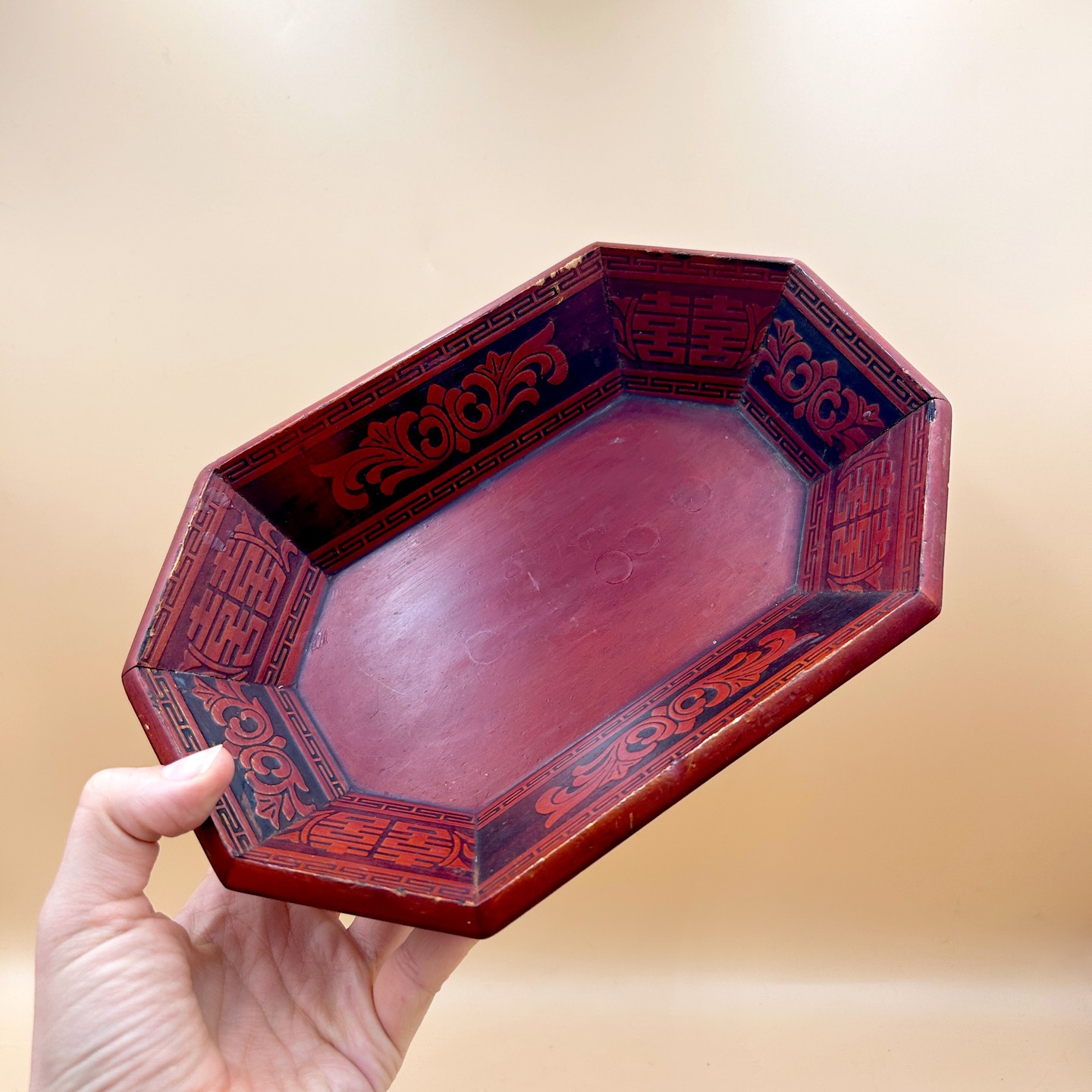 🟢 DOSTĘPNA | Koreańska tacka z laki, Korea, l. 80 XX w.
Ośmioboczna taca z koreańskiej laki (ottchil), wykonana z drewna i pokryta czerwonym lakierem z kontrastową dekoracją w czerni. Wewnętrzne ścianki zdobią stylizowane motywy roślinne, symbole podwójne szczęście (囍, shuāngxǐ) oraz geometryczne bordiury (m.in. wariant wzoru klucza greckiego), typowe dla dekoracyjnej estetyki koreańskiej XX wieku.
Intensywna czerwień symbolicznie wiąże się z pomyślnością i ochroną, co jest częstym znaczeniem w tradycji lakowej Azji Wschodniej.
Konstrukcja z widocznymi łączeniami od spodu wskazuje na ręczne wykonanie, choć o charakterze raczej użytkowo-dekoracyjnym niż ceremonialnym.
Tradycja lakierowania (ottchil) w Korei sięga co najmniej okresu Trzech Królestw (I tys. n.e.), kiedy laką pokrywano przedmioty codzienne i ceremonialne, cenione za trwałość i odporność na wilgoć. W kolejnych epokach, zwłaszcza w czasach dynastii Goryeo i Joseon, rozwinięto wyrafinowane techniki dekoracyjne, takie jak inkrustacja masą perłową (najeonchilgi), które stały się jednym z najważniejszych osiągnięć koreańskiego rzemiosła artystycznego.
Stan bardzo dobry minus - lekkie przetarcia na krawędzi. Drewno paulowni i laka.
25 cm x 17 cm x 6 cm
120 PLN + 15 PLN koszt wysyłki