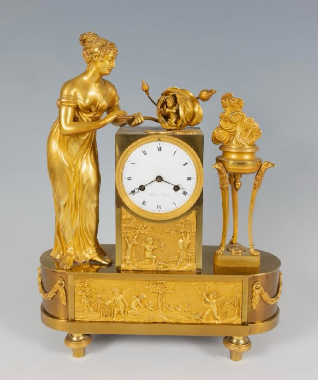 Elegant Empire Period Mantel Clock, France, circa 1825
A superb gilt bronze mantel clock, finely chiseled and mercury-gilded, showcasing all the refinement of the Empire style. This piece features a classically draped female figure, delicately rendered in a graceful pose, holding a floral element above the dial.
The circular white porcelain dial, with Roman numerals, is signed “Pillard à Troyes,” attesting to its high-quality French manufacture. The whole rests on a rectangular base adorned with finely worked bas-reliefs depicting pastoral scenes and putti, characteristic of early 19th-century Neoclassical taste.
On the right, a decorative incense burner element completes the composition harmoniously, adding balance and sophistication to the overall design.
The gilding remains in very good condition, with a rich original patina. Mechanism not tested.
Dimensions:
Height: 45 cm
Width: 35 cm
Depth: 11.5 cm