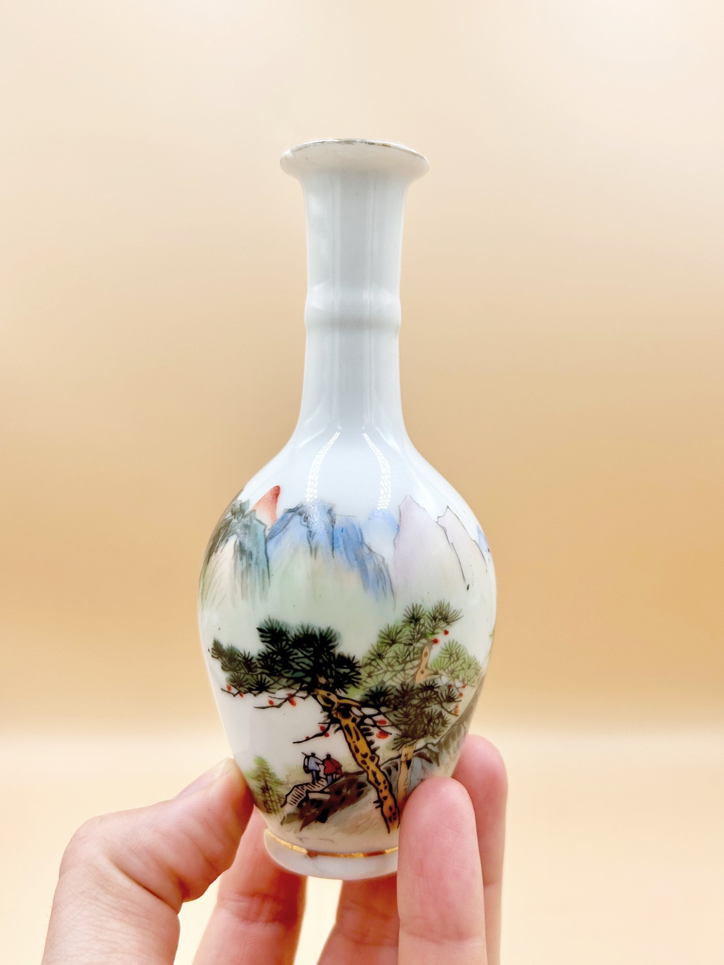 🟢 DOSTĘPNY | Wazonik , Chiny, lata 60. XX w.
Maleńki wazonik z cienkościennej porcelany ręcznie dekorowany, o smukłej szyjce i kulistym brzuścu, solifiore.
Dekoracja została wykonana w technice naszkliwnej, z użyciem delikatnej, „malarskiej” palety barw, przedstawiając pejzaż górski (shan shui) z sosną i niewielką sceną figuralną, co nawiązuje do tradycji chińskiego malarstwa literackiego, lecz w uproszczonej, dekoracyjnej formie. Kompozycja operuje miękkimi przejściami tonalnymi i rozmyciami pigmentu, wskazując wyraźnie na inspirację techniką malarstwa tuszem.
Wys. 14 cm
70 PLN + 15 PLN koszt wysyłki