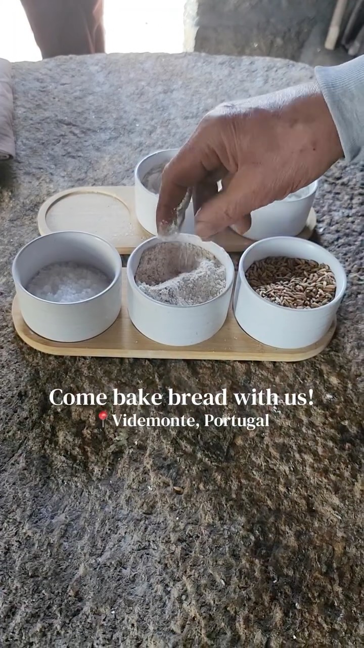 Baking bread in the village of Videmonte turned out to be more than a workshop—we stepped into Senhor Manel’s world. Inside a stone house that he built, Senhor Manel bakes batches of pão de centeio (rye bread) every day. He taught us how, but most importantly he made us feel the pulse of his life in that village. He waved his hand “vamos,” let’s go as the dough was set aside to leaven. Over cobbled streets, he led us to the river to proudly show us an ancient watermill he’s recovering. Later, he poured us homemade grape liqueur “jeropiga,” dug up herbs from his wild garden and shared the teas he makes with each one. As the day’s spring weather started to cool—a reminder that light snow still blanketed the mountain—the coziness of the ovens coaxed us back inside the stone house. A car came to a halt; it was a chatty couple stopping (a ritual) for freshly baked bread. Suddenly, Senhor Manel’s vibrant wife stormed in with baked goodies and the widest and warmest smile. The conversation dragged on…the sun set… Senhor Manel dumped the first hot loaves into a large basket, split one open and smothered it with globs of butter that melted instantly. We didn’t just bake that afternoon; we broke bread with the people of Videmonte. These intimate experiences are exactly what inspire us! Visit portugallesstraveled.com to learn more about who we are and what we do.
#portugal #bakebread #turismodocentro #breadmaking #portuguesetradition