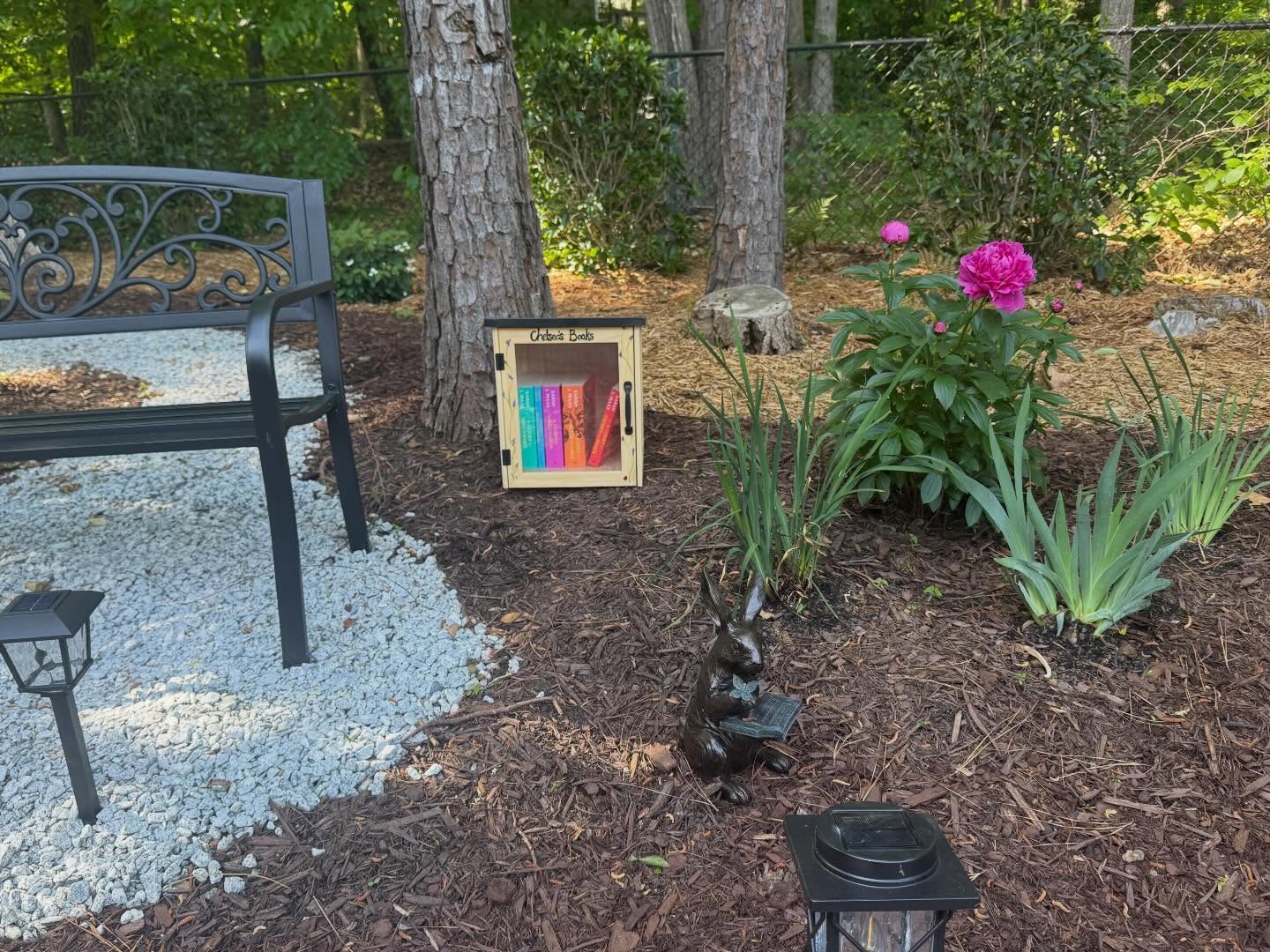 We created a small garden for Chelsea.💙
It has some of her favorite flowers, a quiet place to sit, and a little library filled with books she loved.
I hand-painted the library, on one side it shows her feeding a squirrel, and the other is her with her dog, Lady.
It’s a simple space, but one she would have enjoyed and now a place for us to sit, and remember her. 📚💜🌺