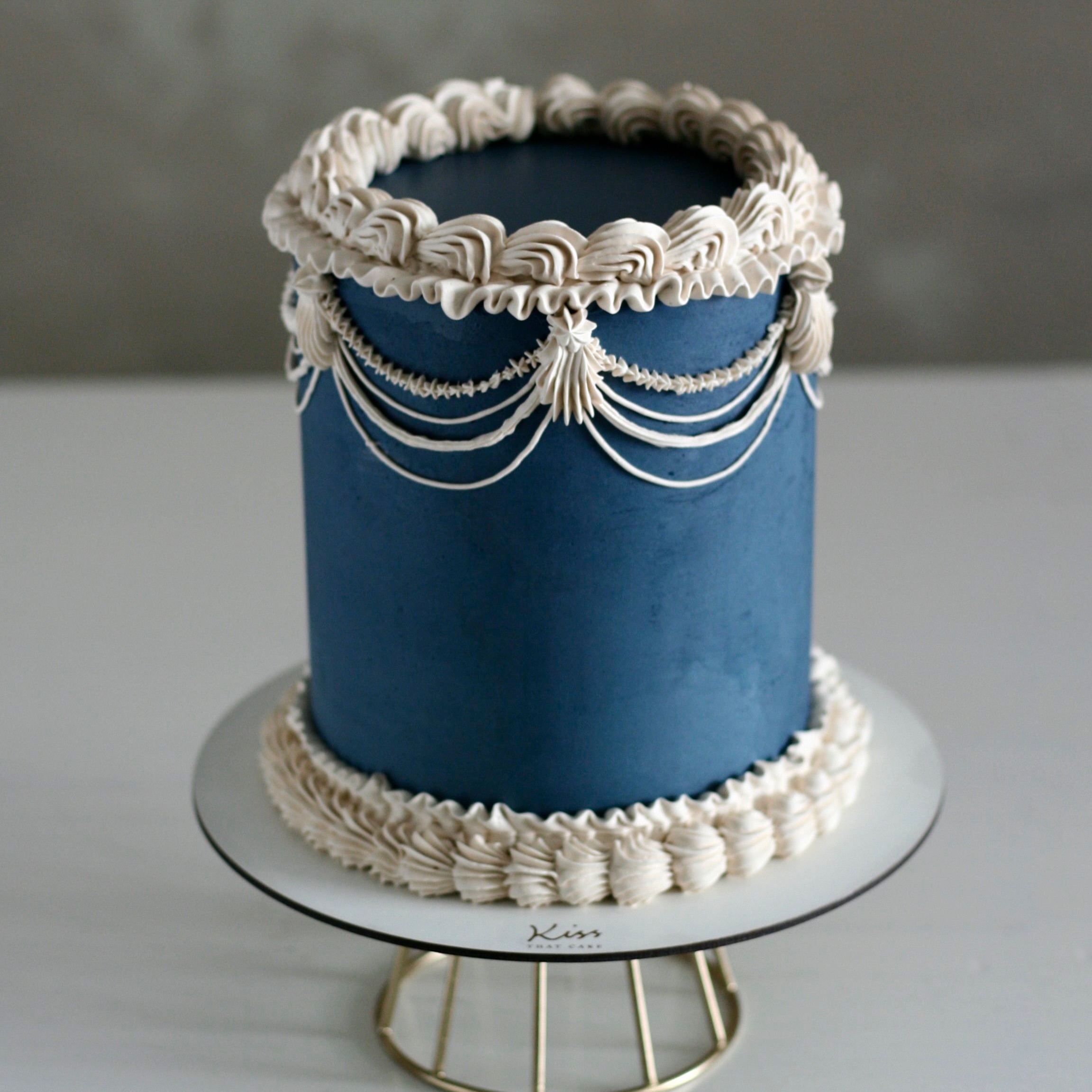 Timeless about deep navy paired with soft ivory.
A palette that feels quietly luxurious, like antique velvet, candlelight, and old money elegance translated into cake form.
Dark buttercream behaves completely differently from lighter colors. The smoothing technique is far less forgiving, because deep shades can’t really be patched or corrected without leaving marks or uneven texture behind.
And once the ivory piping begins, there’s no second chance.
One misplaced detail means wiping it away, but on a dark surface, every touch leaves a trace. So each line has to be piped with confidence, clean movement, and no room for error.
Some cakes look simple.
The people who make them know they’re often the hardest ones.