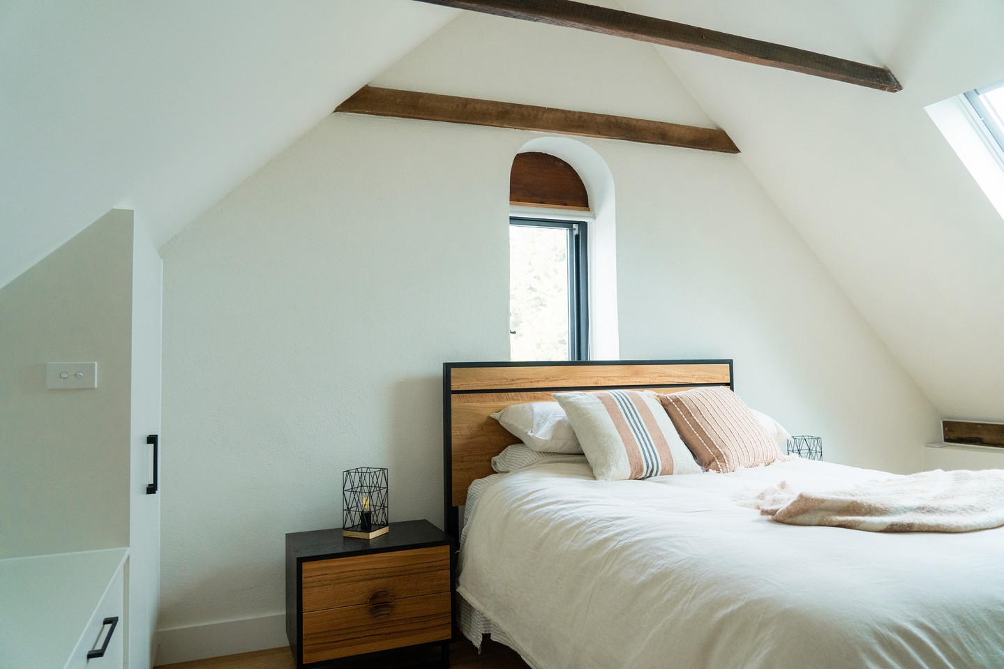 The mezzanine bedroom in a converted bluestone stables, original timber beams left exposed in the raked ceiling, an arched window detail carried through from the building's origins, and a skylight added to bring natural light into the upper level. Modern finishes throughout without losing what made the structure worth keeping.
#buildtrendhomes #macedonrangesbuilder #heritagerestoration #conversionproject #regionalvictoria