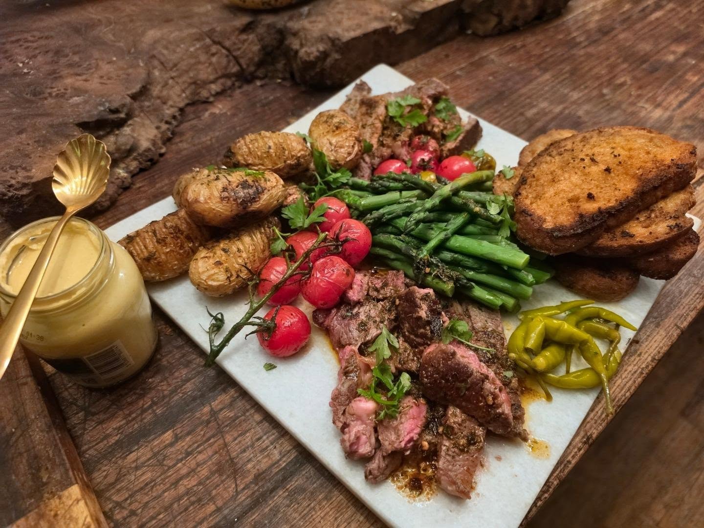 Casual little sharing platter piled with Rib Eye, Garlic Hasselback Potatoes, Pan Roasted Cherry Tomatoes, Asparagus & Garlic Toast 🩷