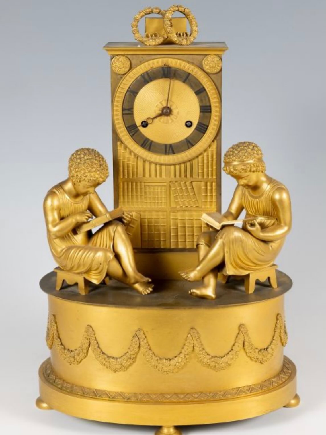 Elegant mantel clock in finely chased mercury-gilt bronze, illustrating the refined taste of the Restoration period for allegorical subjects inspired by education and the arts. Known as “The Library,” this model depicts two young readers seated on either side of an imposing bookcase filled with books. The composition symbolizes study, the transmission of knowledge, and the awakening of intellectual curiosity from an early age. The delicate treatment of the faces, the naturalistic rendering of the drapery, and the richness of the decorative details testify to the high quality of craftsmanship of this work.
The circular dial with Roman numerals is integrated into a stylized library cabinet whose shelves are filled with carefully detailed volumes. The ensemble rests on a circular base adorned with relief garlands, emphasizing the harmony and balance of the composition. The remarkable mercury gilding, characteristic of high-end French productions from the first third of the 19th century, has retained all its depth and brilliance, highlighting the fineness of the chasing.
The movement is in working order and comes complete with its winding key.
Period: Restoration, circa 1830
Origin: France
Material: Mercury-gilt bronze
Dimensions: H. 45 cm × W. 28 cm × D. 18.5 cm
Condition: Very good state of preservation; movement in working order
Accessories: Original winding key present. #yesterdayknuts #antiqueclock #antique #antiquedealersofinstagram #homedecor