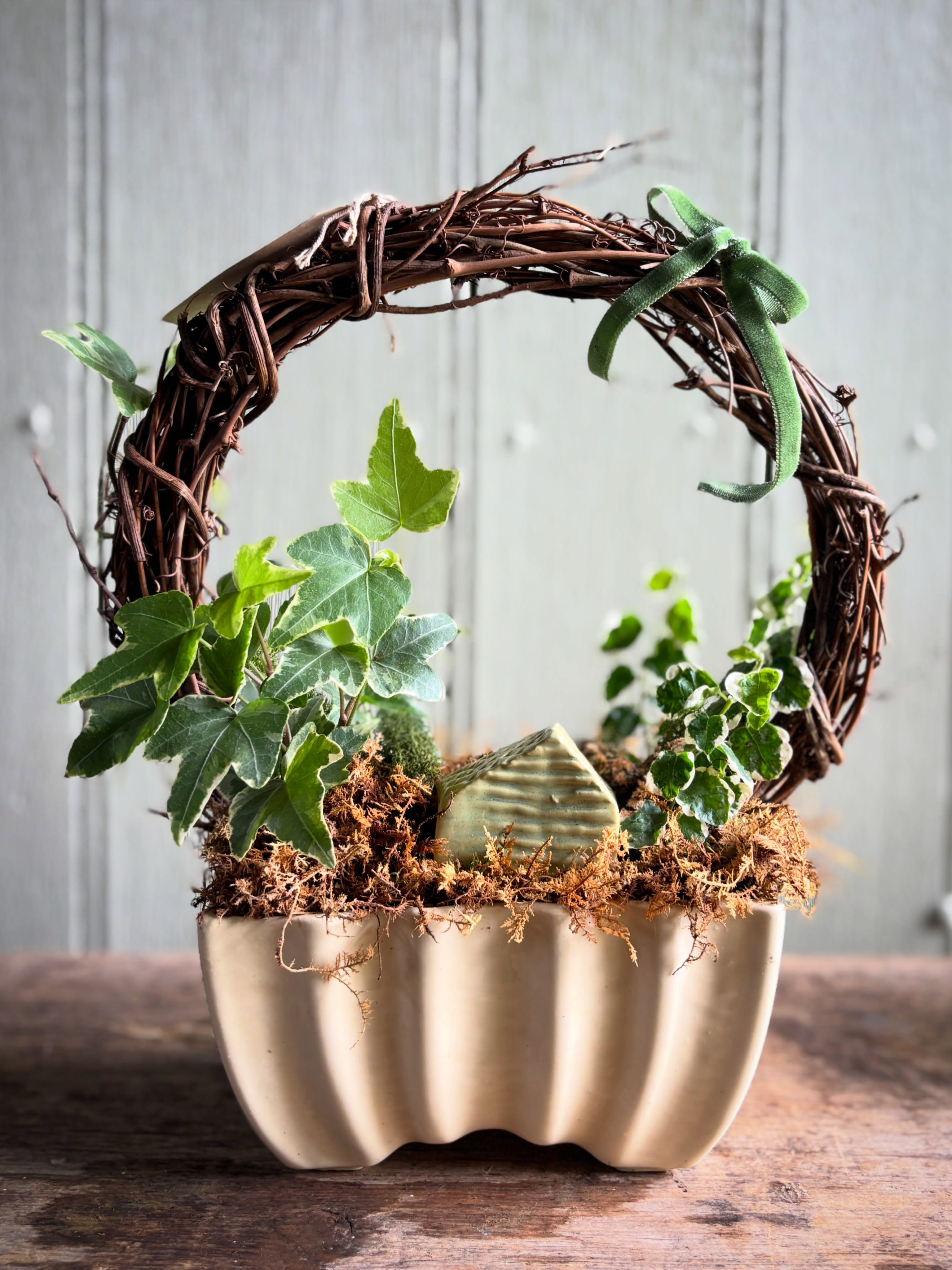 "Waiting for a Move In Date" features a tiny ceramic house (made by local potter Mossy Trail Ceramics) nestled in a lush houseplant setting.
Trailing Ivy and Creeping Fig will travel around the grapevine wreath form creating a beautiful and whimsical piece.
Vintage ceramic pot is soft buttery yellow.
Watch this piece evolve over time and over-winter for multi-season joy.
Available now for pick up at the Flower Truck
Visit the website to preorder and pick up at your convenience or peruse other pretty topiary options.