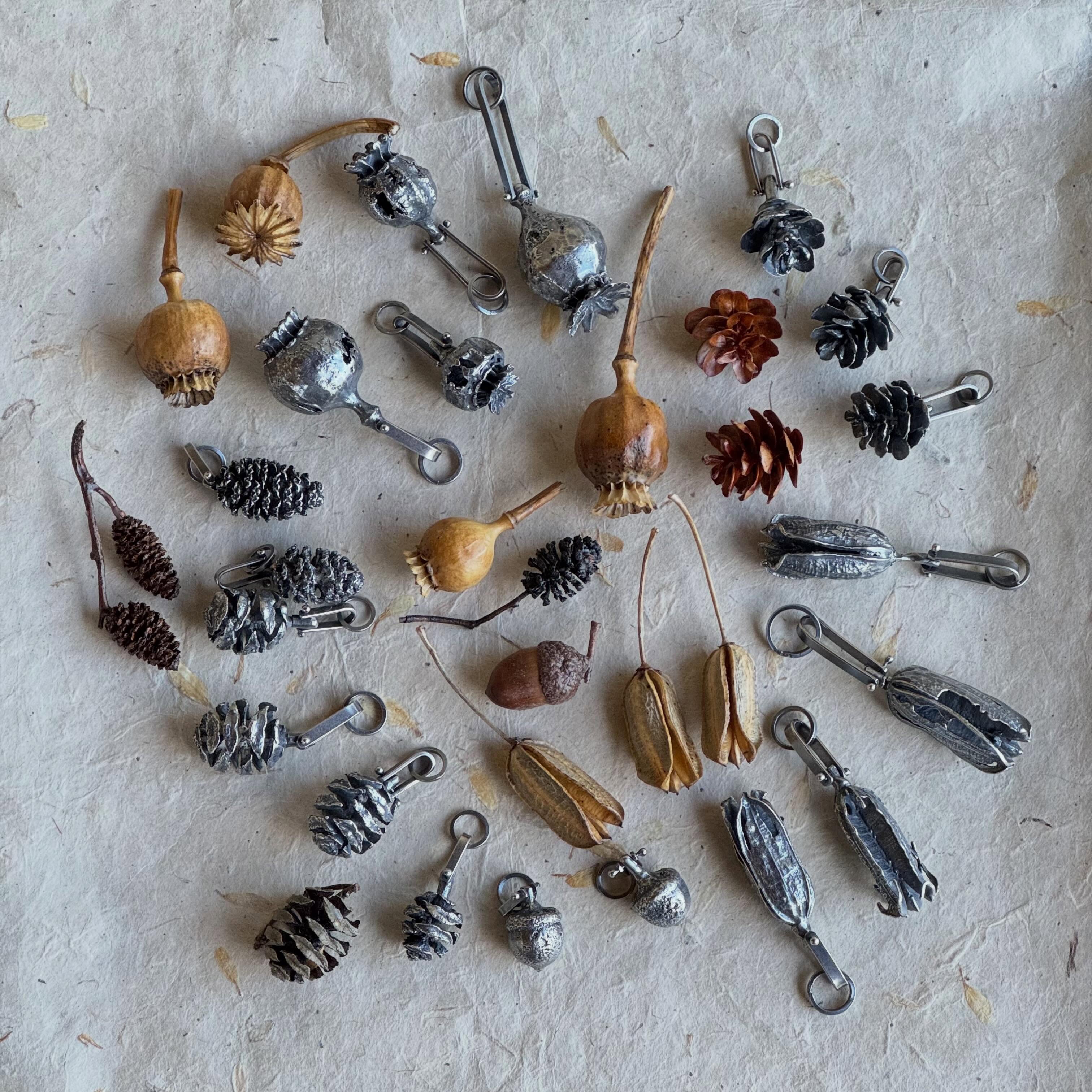 I’ve been casting cones and pods and making hinges for these pendants that I will be bringing to shows this summer. #sequoia #alder #acorns #poppypods #hemlock. If you see one you love, let me know. I will also list these on my website so if you aren’t on my mailing list, head over to the link in my profile to sign up.
Being able to collect in my garden and out on walks makes me slow down and really look at the details. Have you ever really inspected the top of a poppy pod and the way the sequoia cone is so geometrical? Casting them is a great way to capture the intricacies. It is always a guessing game to see which plants, cones and pods translate well into silver. My other challenge is remembering where I collected them and what they are. Those pods in the lower right are some that I think I found near Tucson. I thought they were agave pods, but then this year I found some agave pods and they are a little bit different. Anyone know?