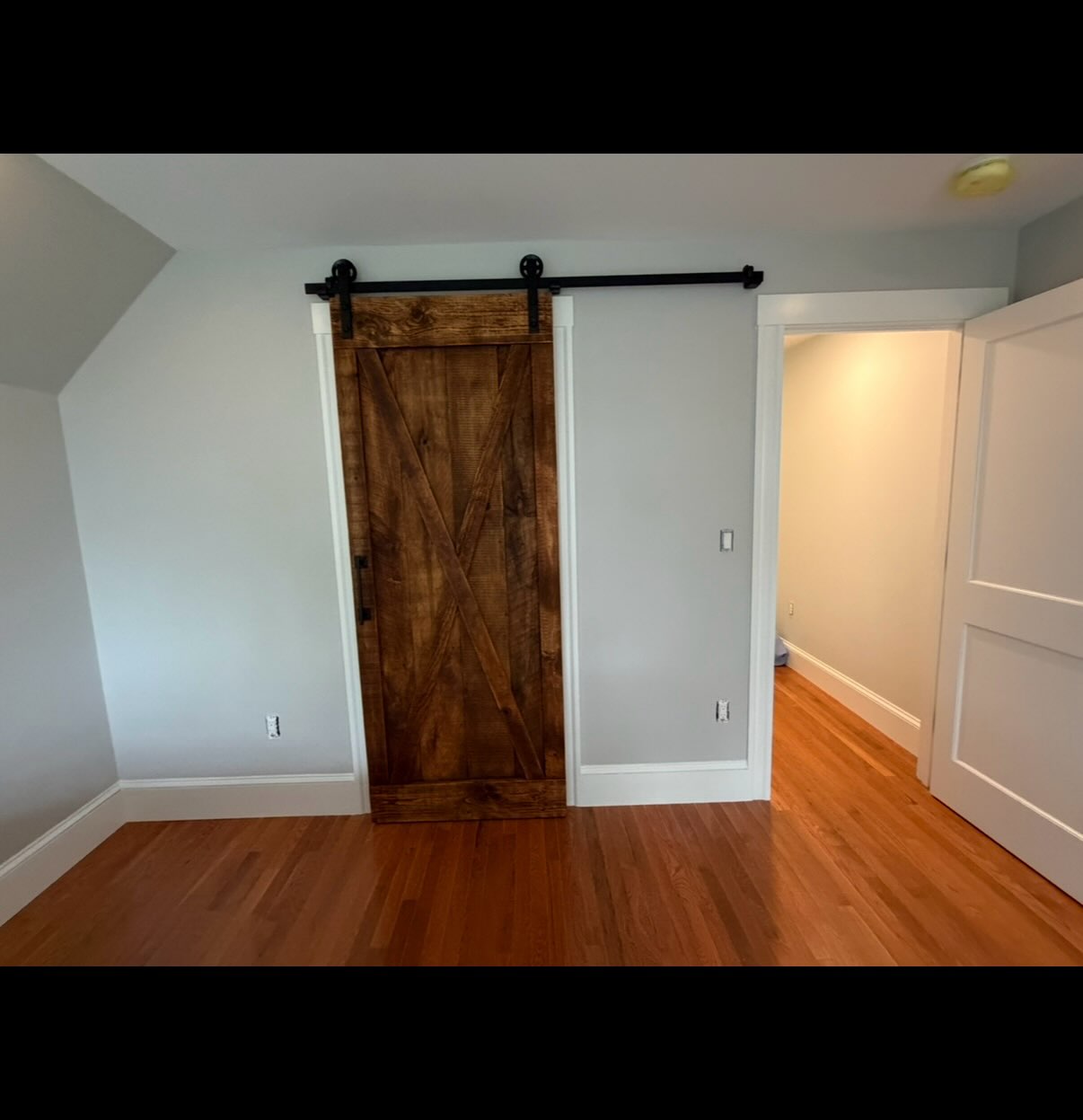 Neal and his family from Swampscott, MA had done extensive renovations to expand their 100+ year olde New England home and added a master bedroom in the back upstairs. This room has a spacious bathroom with laundry and it needed a sliding barn door for function and style.
The Barndoorist worked with Neal and his builder, as the space had angled ceilings and required exacting calculations to make it fit just right. We wanted the door to slide to a point where it did not go over the wide decorative casing of the room’s main entryway. But at the same time, it had to be wider than the bathroom entryway, and not wider than that room’s casing.
This is a situation where, when the door is closed, you can still see some of the decorative left and right vertical casing but the door and its added side board features close the space and provide privacy with style.
We used the hidden floor guide and everything worked out wonderfully with a rustic door that had a customized wax coating which close-matched the floor coloring.
#swamscott #marblehead #salem #nahant #Beverly