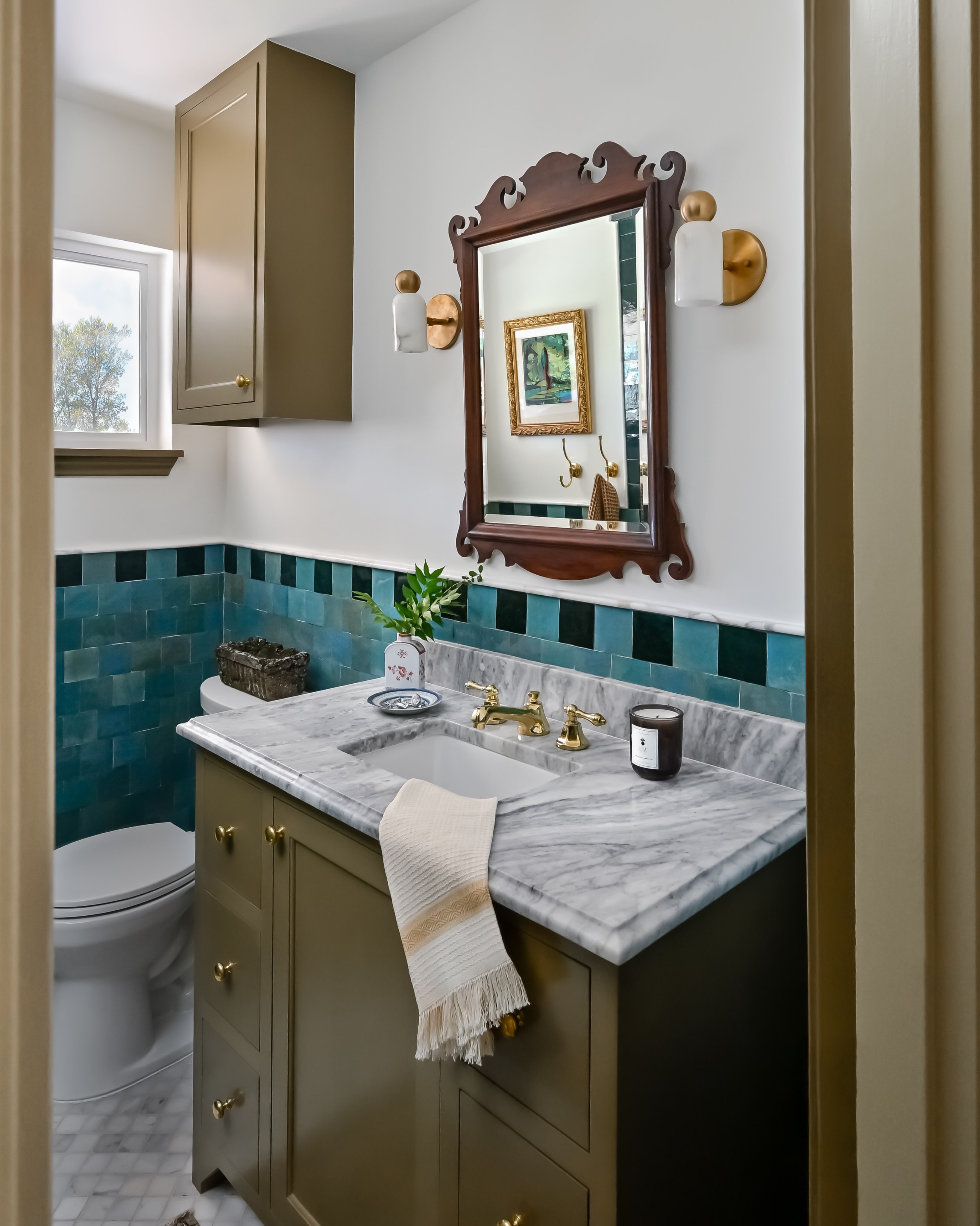 We’re drawn to tile that adds character without taking over. Here, the two-tone teal creates just enough contrast against the earthy green cabinetry, while the antique dark wood mirror brings in warmth and grounds the space.
That mix of color, contrast, and slightly unexpected pairings is exactly what gives the Eclectic Cottage its name (and this little bathroom so much personality!)
